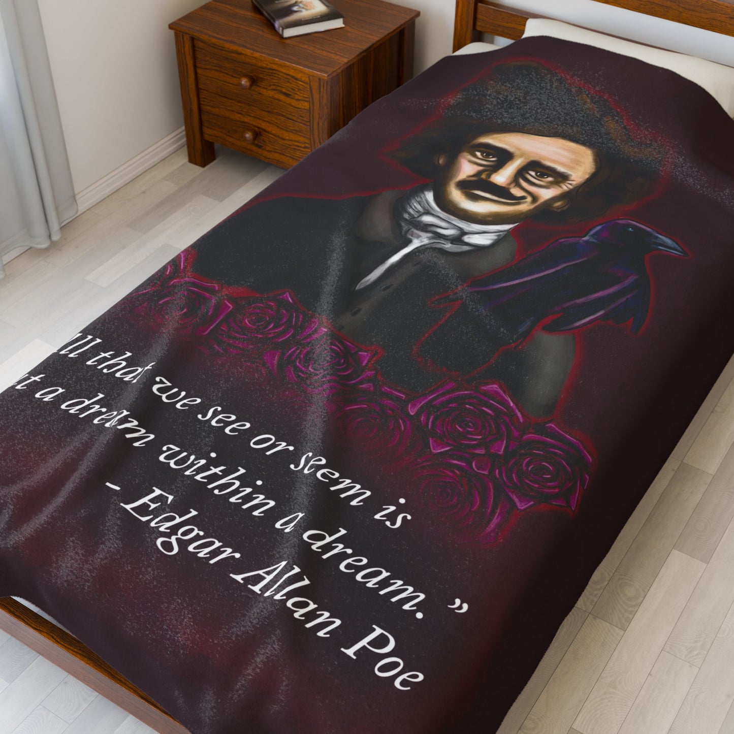 A large burgundy velveteen plush blanket featuring a smirking Edgar Allan Poe, a brooding raven, and crimson roses—perfect for cozying up with your favorite haunting thoughts and the poetic quote, "All that we see or seem is but a dream within a dream. Shown on a twin size bed.