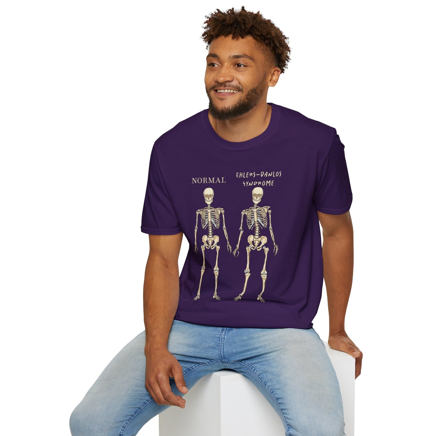 Man wearing a dark purple unisex short sleeve t-shirt featuring two skeletons side by side—one labeled "normal," the other "Ehlers-Danlos Syndrome"—because connective tissue disorders deserve more visibility (and maybe a sense of humor, too).