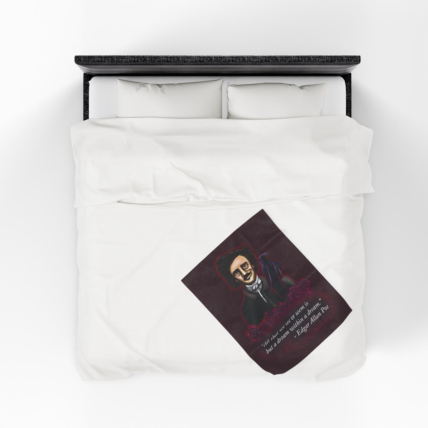 A small burgundy velveteen plush blanket featuring a smirking Edgar Allan Poe, a brooding raven, and crimson roses—perfect for cozying up with your favorite haunting thoughts and the poetic quote, "All that we see or seem is but a dream within a dream. Shown on a queen size bed from above.