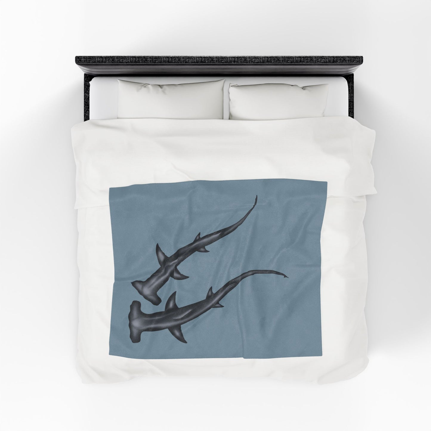 A medium blue-grey velveteen plush blanket featuring two hammerhead sharks gliding through the fabric like it's their personal ocean—perfect for wrapping yourself in comfort with a side of bite. Shown on a queen size bed from above.