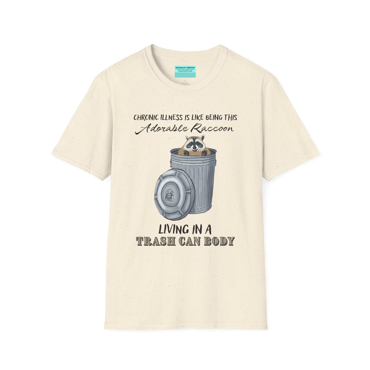 Beige t-shirt featuring an illustration of a raccoon in a metal trash can, with the phrase 'Chronic illness is like being this adorable raccoon living in a trash can body' printed on it.