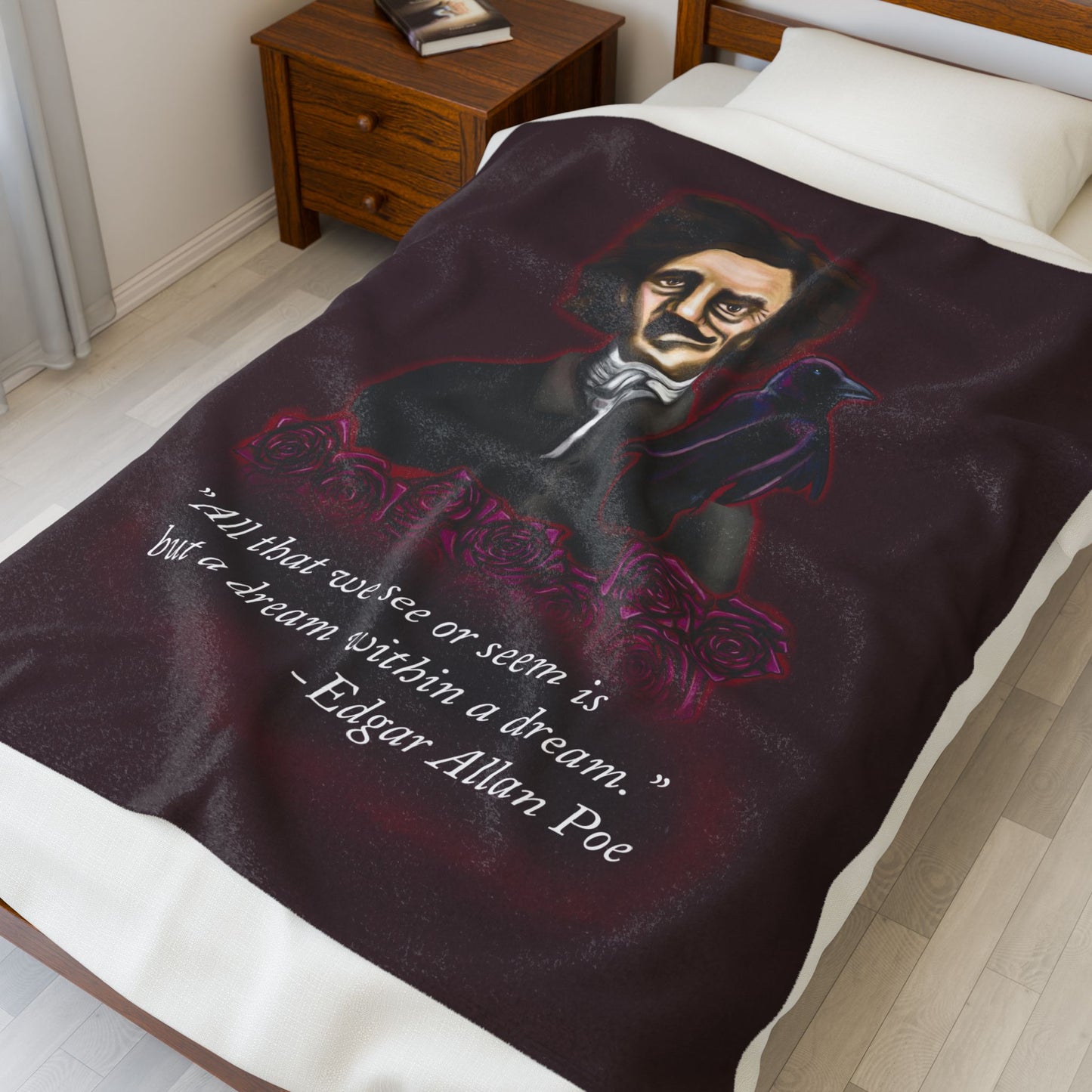A medium burgundy velveteen plush blanket featuring a smirking Edgar Allan Poe, a brooding raven, and crimson roses—perfect for cozying up with your favorite haunting thoughts and the poetic quote, "All that we see or seem is but a dream within a dream. Shown on a twin size bed.