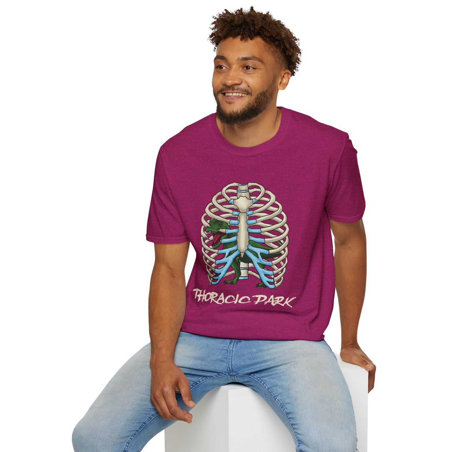 Man wearing a pink unisex short sleeve tee with a clever Jurassic twist—an anatomical rib cage doubles as a prehistoric prison for a tiny T-Rex, with the punny caption "Thoracic Park" below. It's dino-mite meets anatomy class in the best way possible.
