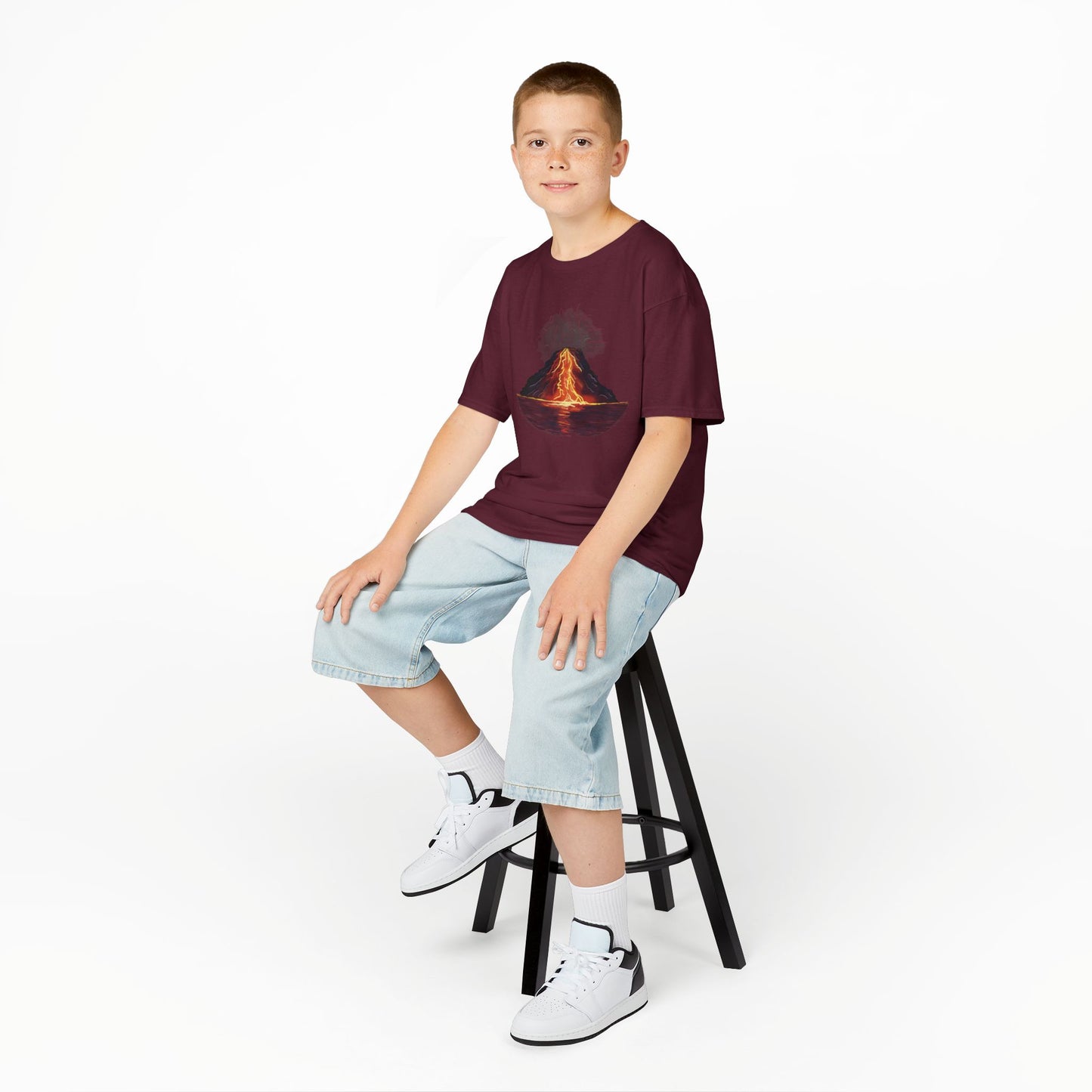 A boy wearing a burgundy kid's t-shirt featuring a fiery illustration of an erupting volcano—because even the most explosive adventures start with a great outfit!