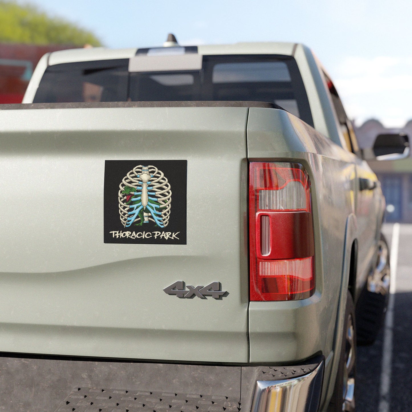 Square black magnet on the back of a pick-up truck featuring a rib cage with a T-Rex trapped inside; bold text reads “Thoracic Park” in a playful nod to classic dinosaur thrillers and chest anatomy.