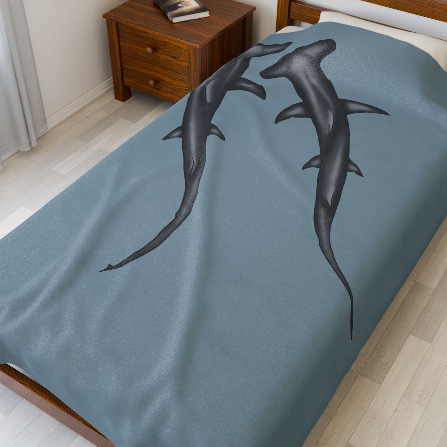 A large blue-grey velveteen plush blanket featuring two hammerhead sharks gliding through the fabric like it's their personal ocean—perfect for wrapping yourself in comfort with a side of bite. Shown on a twin size bed.