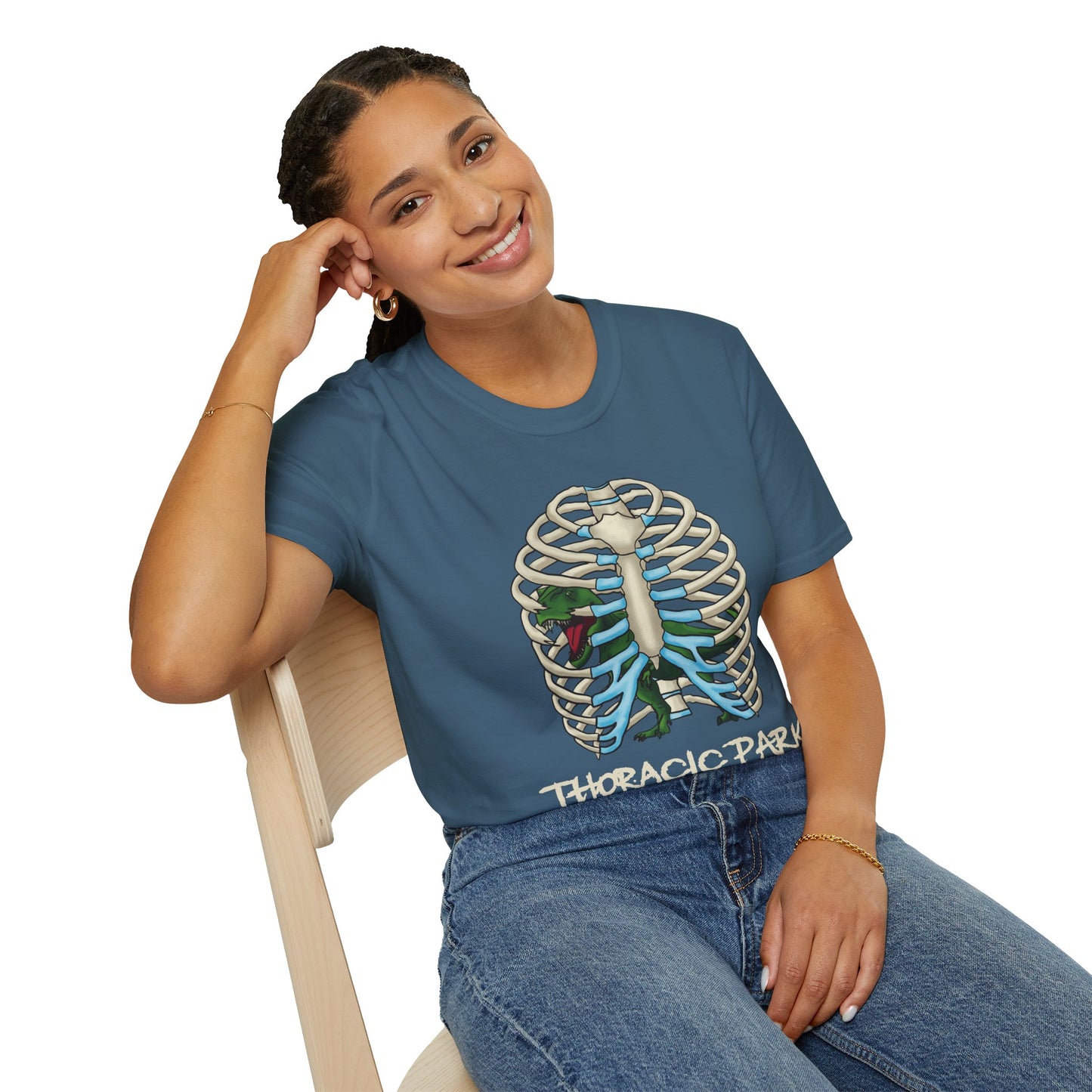 Woman wearing an indigo blue unisex short sleeve tee with a clever Jurassic twist—an anatomical rib cage doubles as a prehistoric prison for a tiny T-Rex, with the punny caption "Thoracic Park" below. It's dino-mite meets anatomy class in the best way possible.