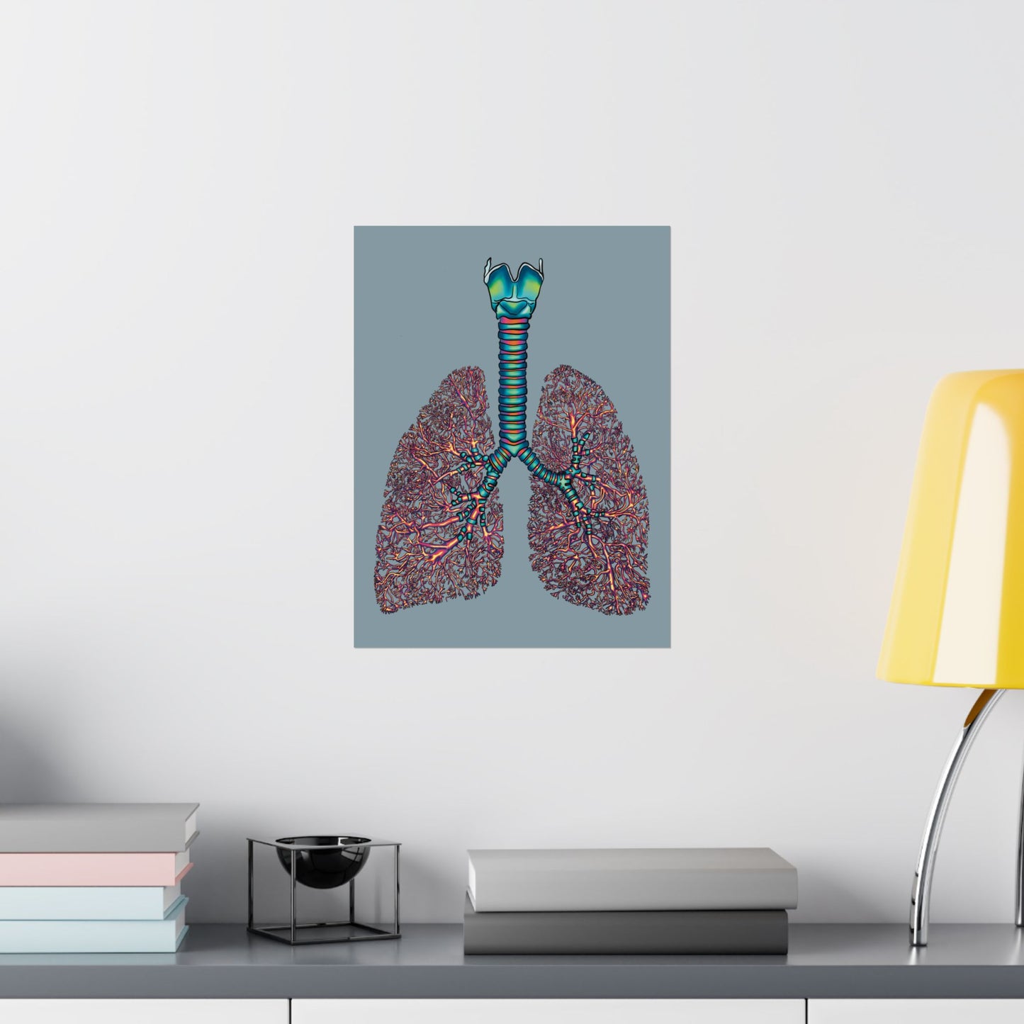 Small poster displayed on a wall in an office setting, featuring an illustration of anatomical lungs with detailed bronchial tree, trachea, and larynx, set against a blue-grey background.