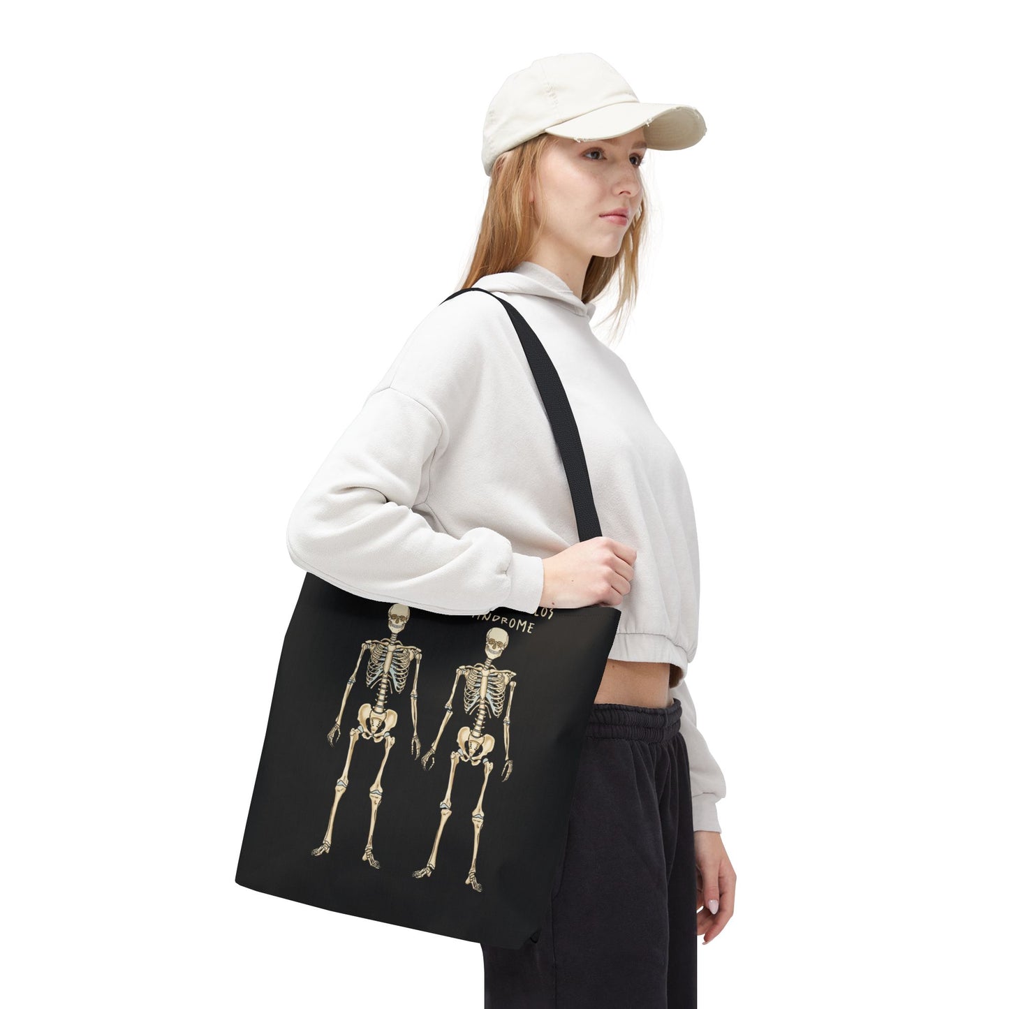Black tote bag is over a woman's shoulder. The tote displays two skeletons side by side. The first is labeled 'Normal' and the second is labeled 'Ehlers-Danlos Syndrome,' visually illustrating the skeletal effects of EDS.