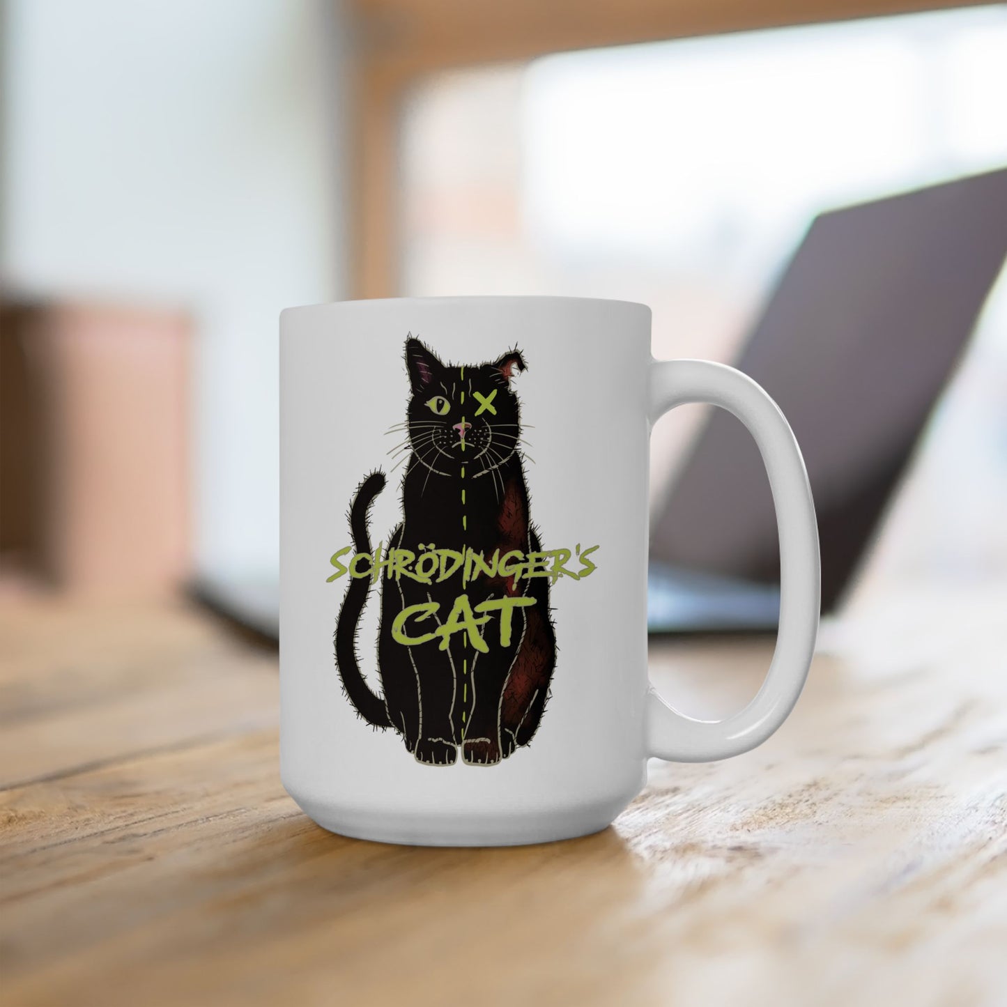 Right view of large white coffee mug featuring a drawing of a black cat that is alive on one half and dead on the other, with the text 'Schrödinger's Cat' printed across the image. The mug is on a table next to an open laptop.