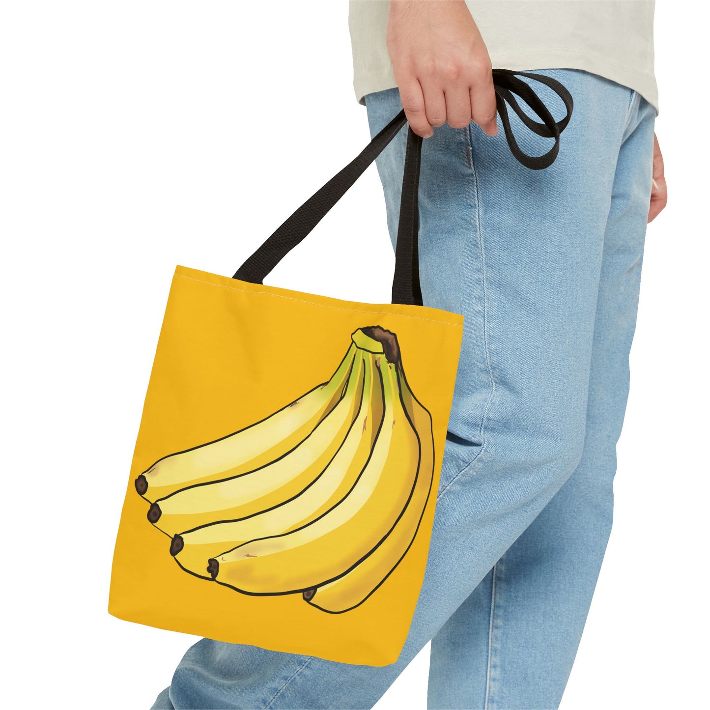 Person holding a medium yellow tote bag featuring a playful illustration of a bunch of bananas on the front, set against a solid yellow background.
