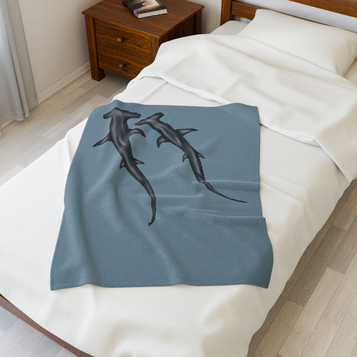 A small blue-grey velveteen plush blanket featuring two hammerhead sharks gliding through the fabric like it's their personal ocean—perfect for wrapping yourself in comfort with a side of bite. Shown on a twin size bed.