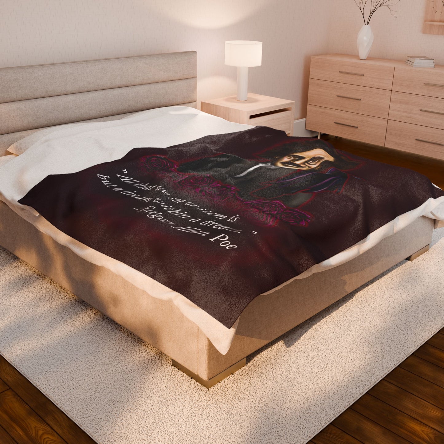 A large burgundy velveteen plush blanket featuring a smirking Edgar Allan Poe, a brooding raven, and crimson roses—perfect for cozying up with your favorite haunting thoughts and the poetic quote, "All that we see or seem is but a dream within a dream. Shown on a queen size bed.