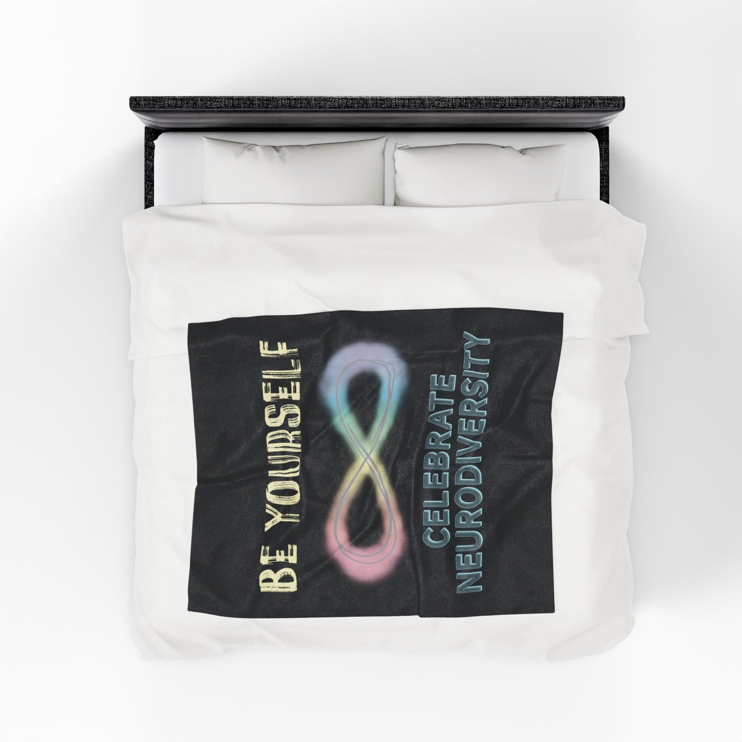 A medium black velveteen plush blanket with a pastel rainbow infinity symbol and the uplifting phrase "Be yourself, celebrate neurodiversity"—soft enough to soothe your senses, bold enough to make a statement. Shown on a queen size bed.