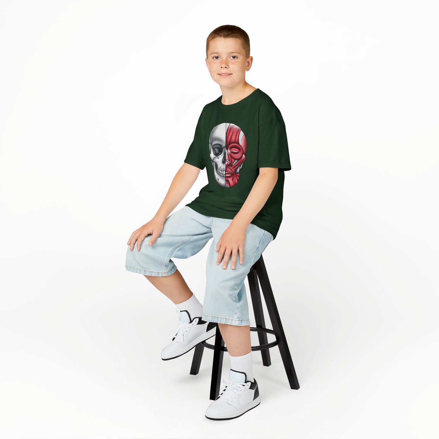 A boy wearing a forest green kids' t-shirt featuring an anatomical drawing of a human skull, with facial muscles illustrated on one half of the skull.
