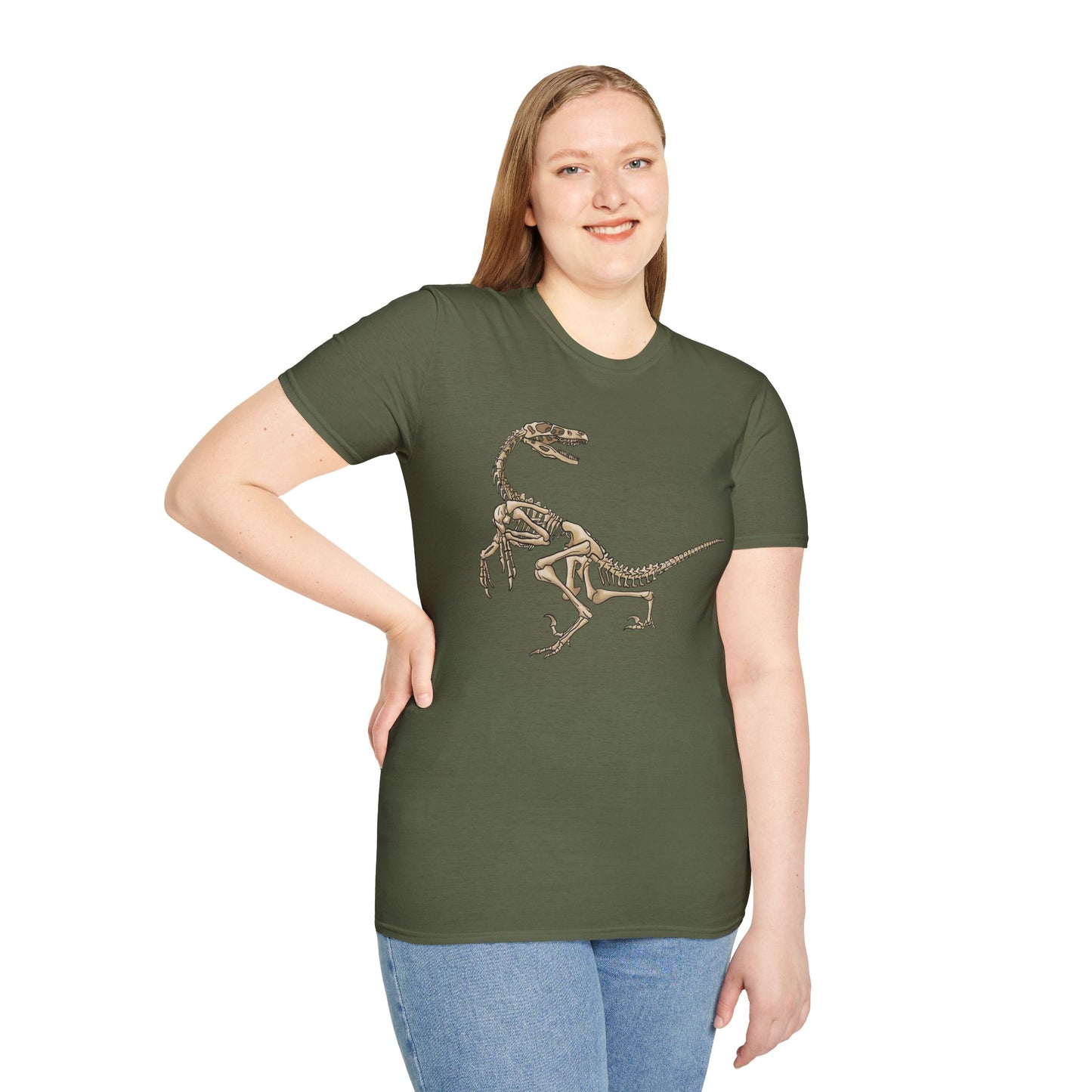 Woman wearing a military green unisex short sleeve t-shirt with a fierce velociraptor skeleton strutting across the chest—because who says extinct can’t be stylish?