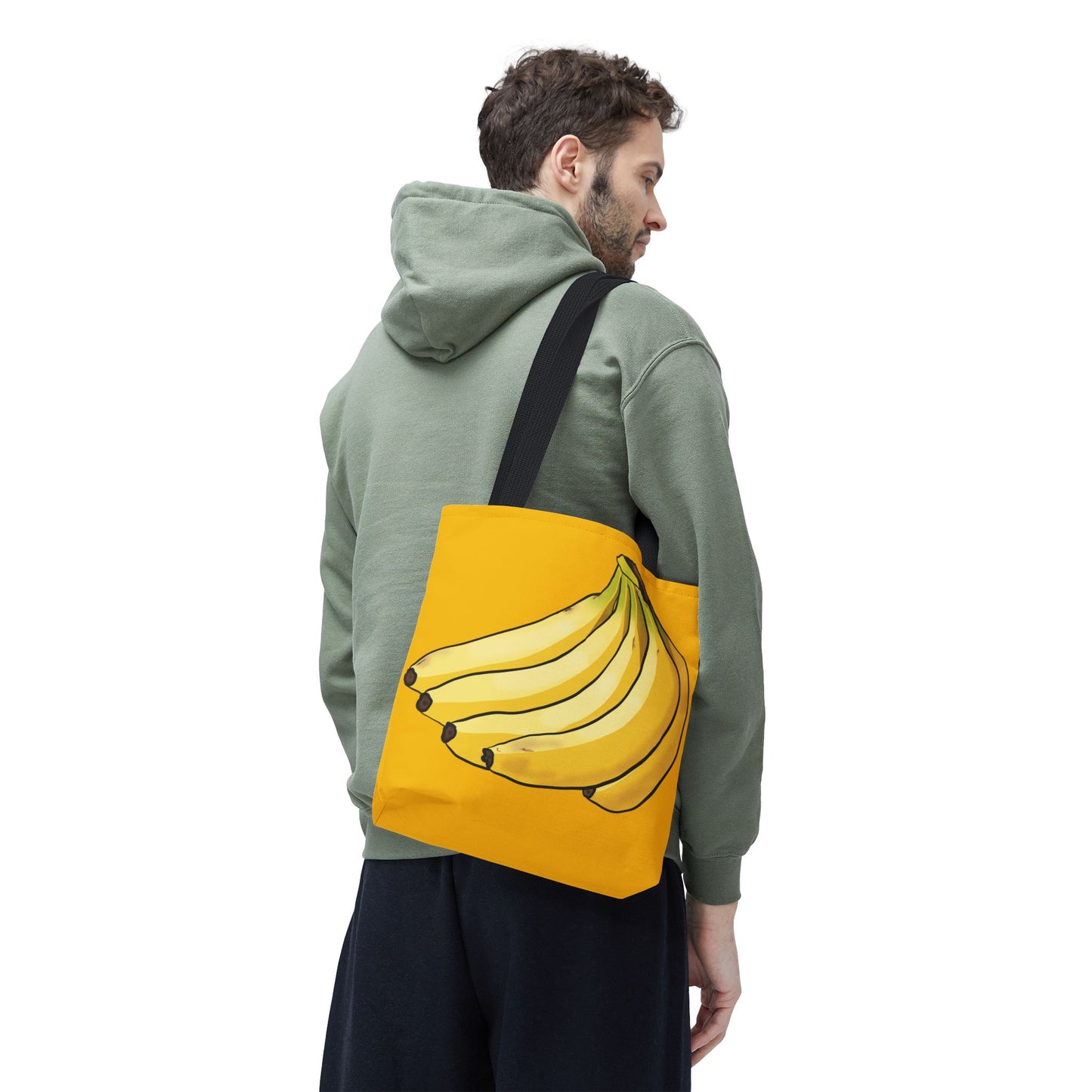 Man carrying a small yellow tote bag featuring a playful illustration of a bunch of bananas on the front, set against a solid yellow background.