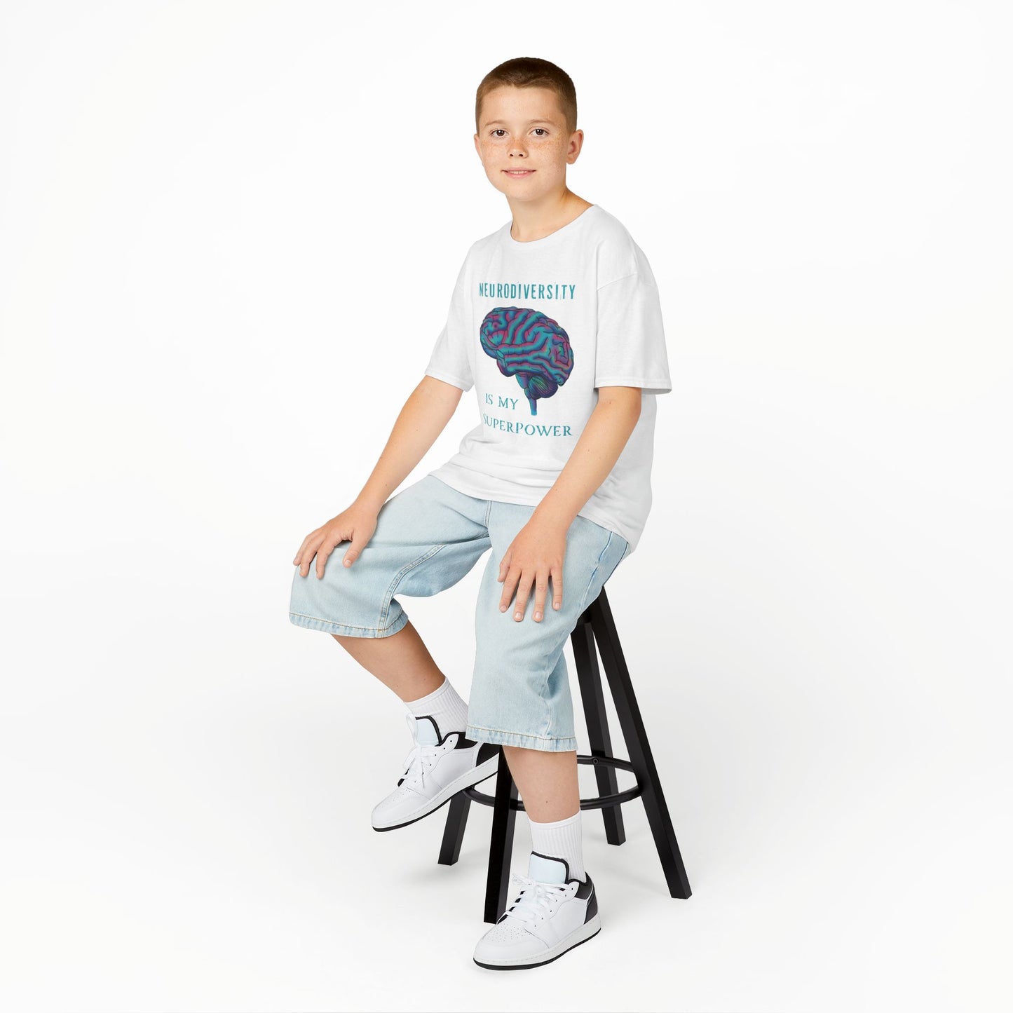 Boy is wearing a white unisex kids' t-shirt featuring a drawing of an anatomical brain and the text 'Neurodiversity is my superpower.'