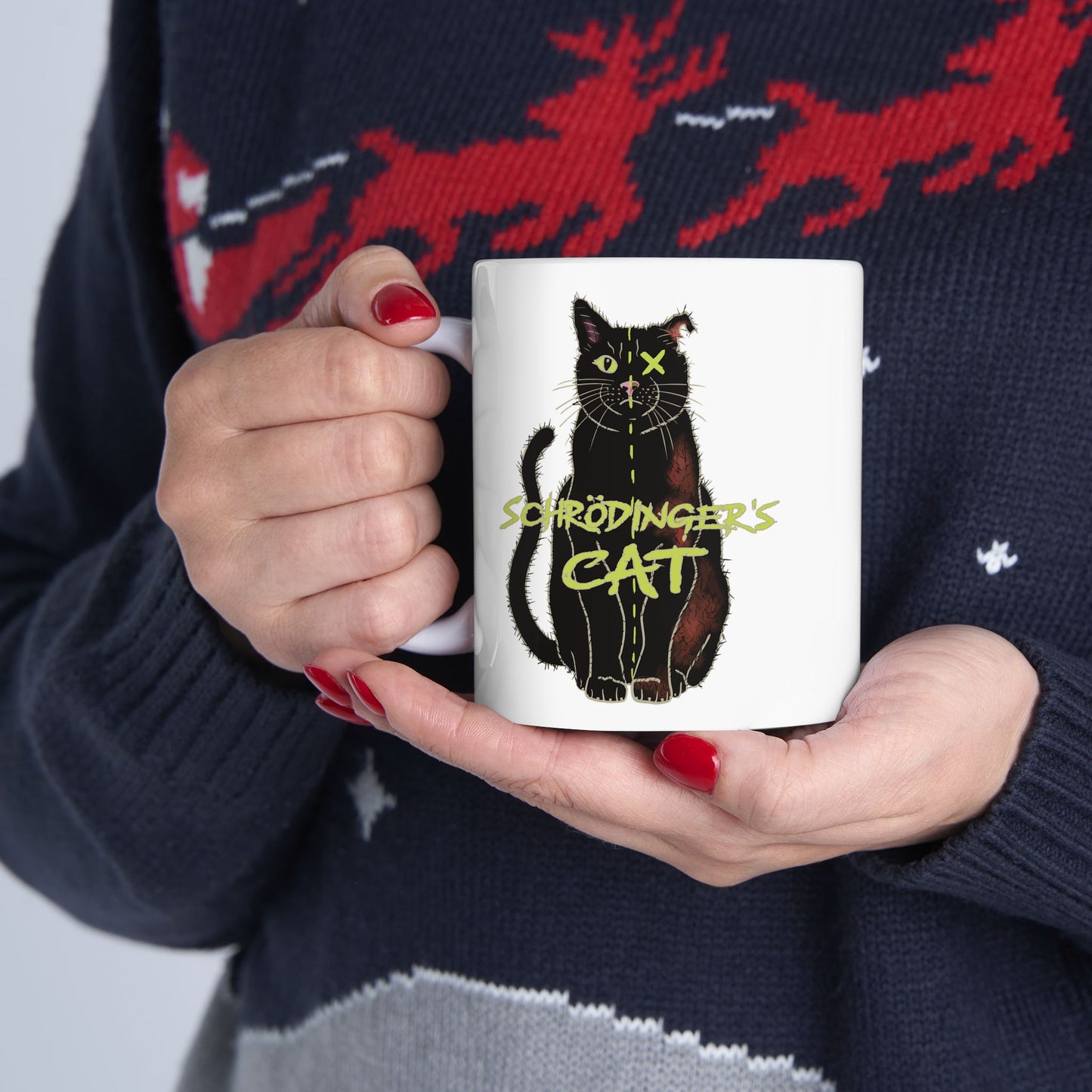 A woman is holding a white coffee mug featuring a drawing of a black cat that is alive on one half and dead on the other, with the text 'Schrödinger's Cat' printed across the image.