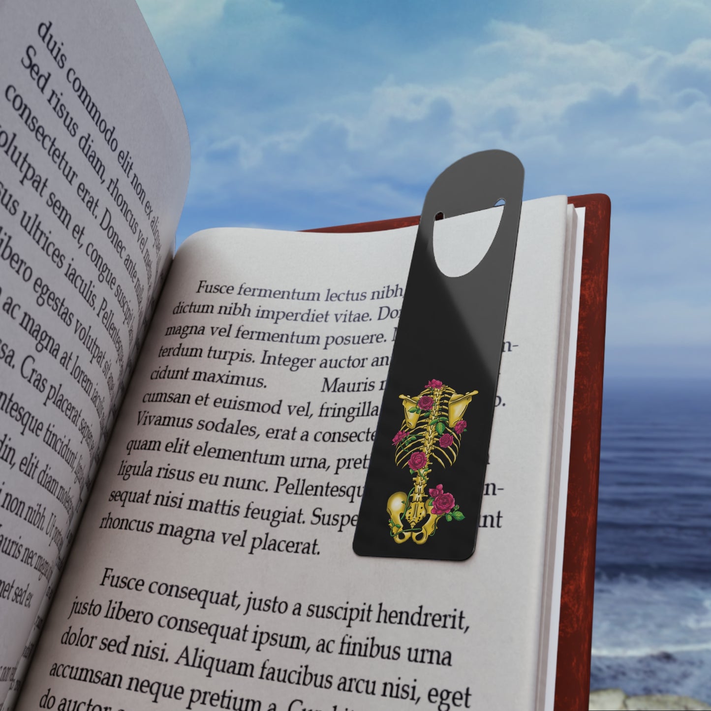 Black aluminum bookmark clipped in a book featuring a gold anatomical skeleton with vibrant pink roses entwined around the bones, creating a striking blend of macabre and botanical elegance.