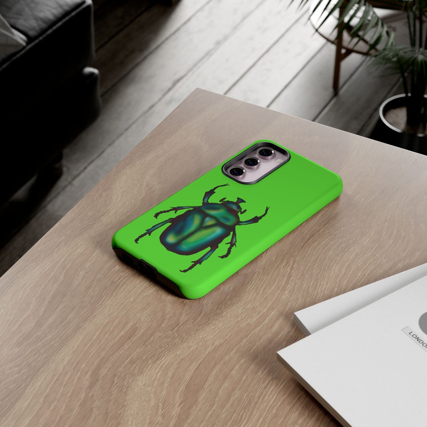 Lime green phone case featuring a dazzling illustration of a green and blue June bug—this iridescent little beetle brings all the shine without the buzz. The case is shown in use sitting on a table.