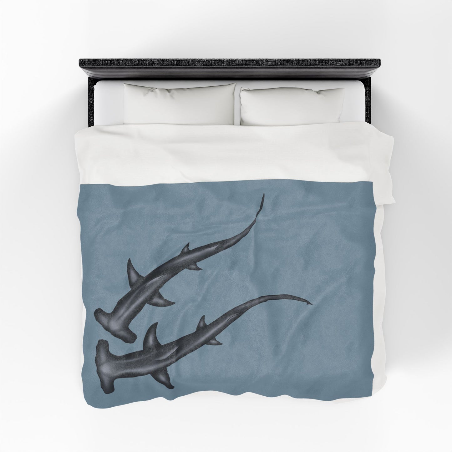 A large blue-grey velveteen plush blanket featuring two hammerhead sharks gliding through the fabric like it's their personal ocean—perfect for wrapping yourself in comfort with a side of bite. Shown on a queen size bed from above.