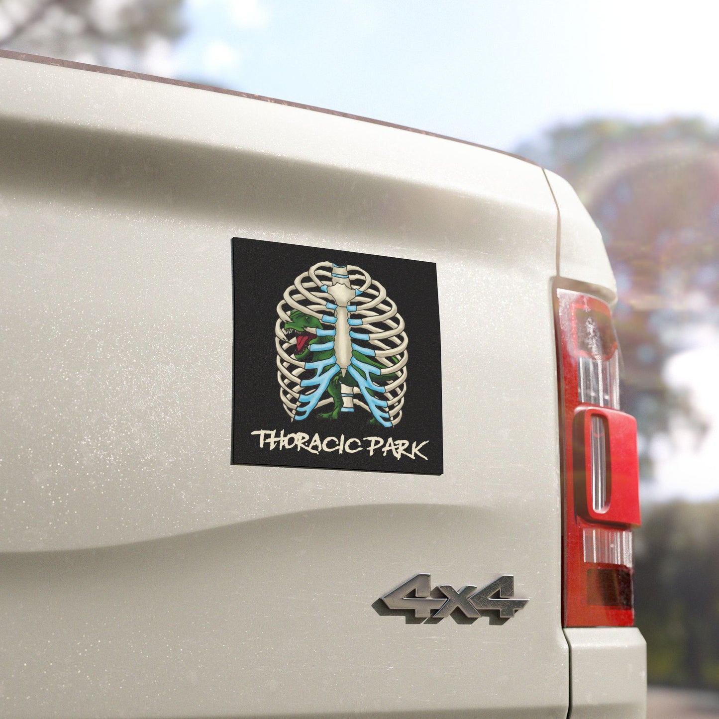 Close up view of a black magnet  on the back of a pick-up truck featuring a rib cage with a T-Rex trapped inside; bold text reads “Thoracic Park” in a playful nod to classic dinosaur thrillers and chest anatomy.
