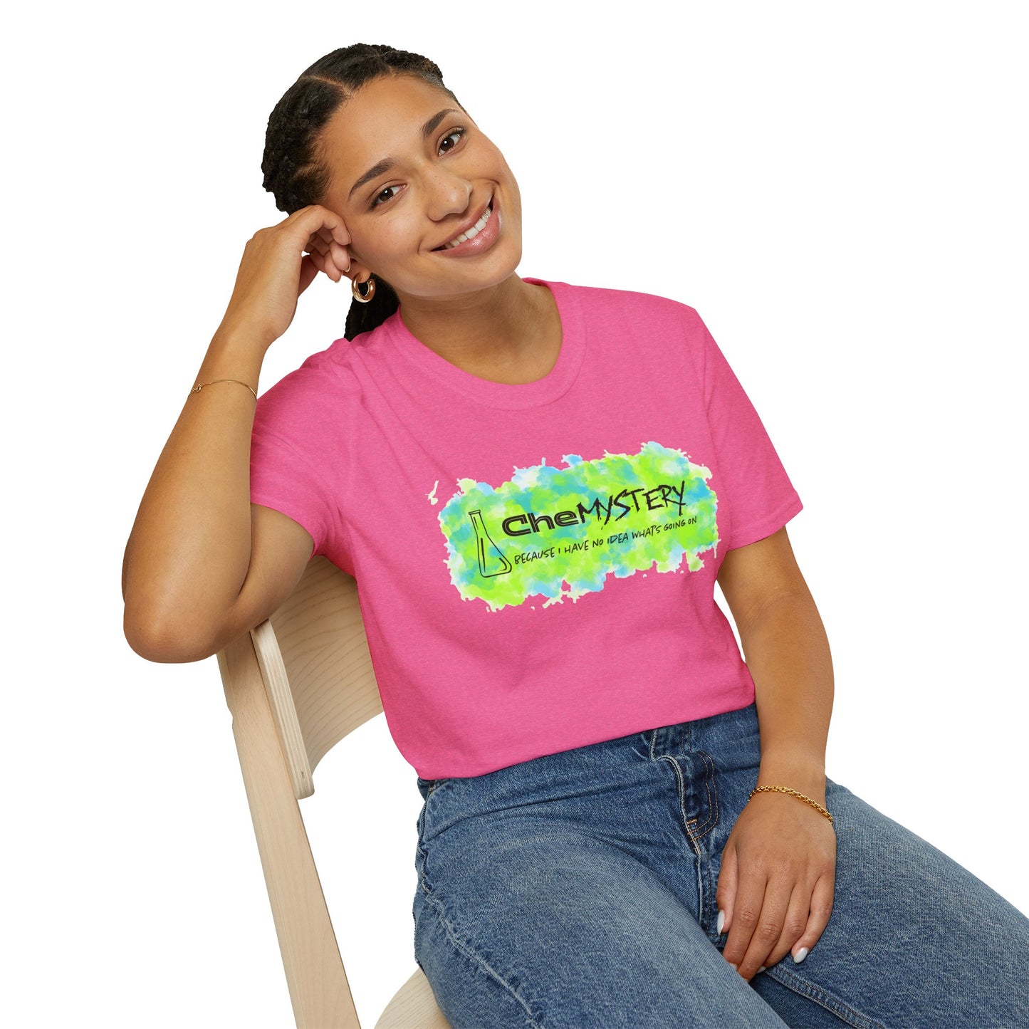 Woman wearing a pink short-sleeve unisex t-shirt with playful watercolor-style blue and green splotches, a simple line-drawn beaker, and the witty phrase “CheMystery: because I have no idea what’s going on”—perfect for anyone who’s ever been personally victimized by the periodic table.