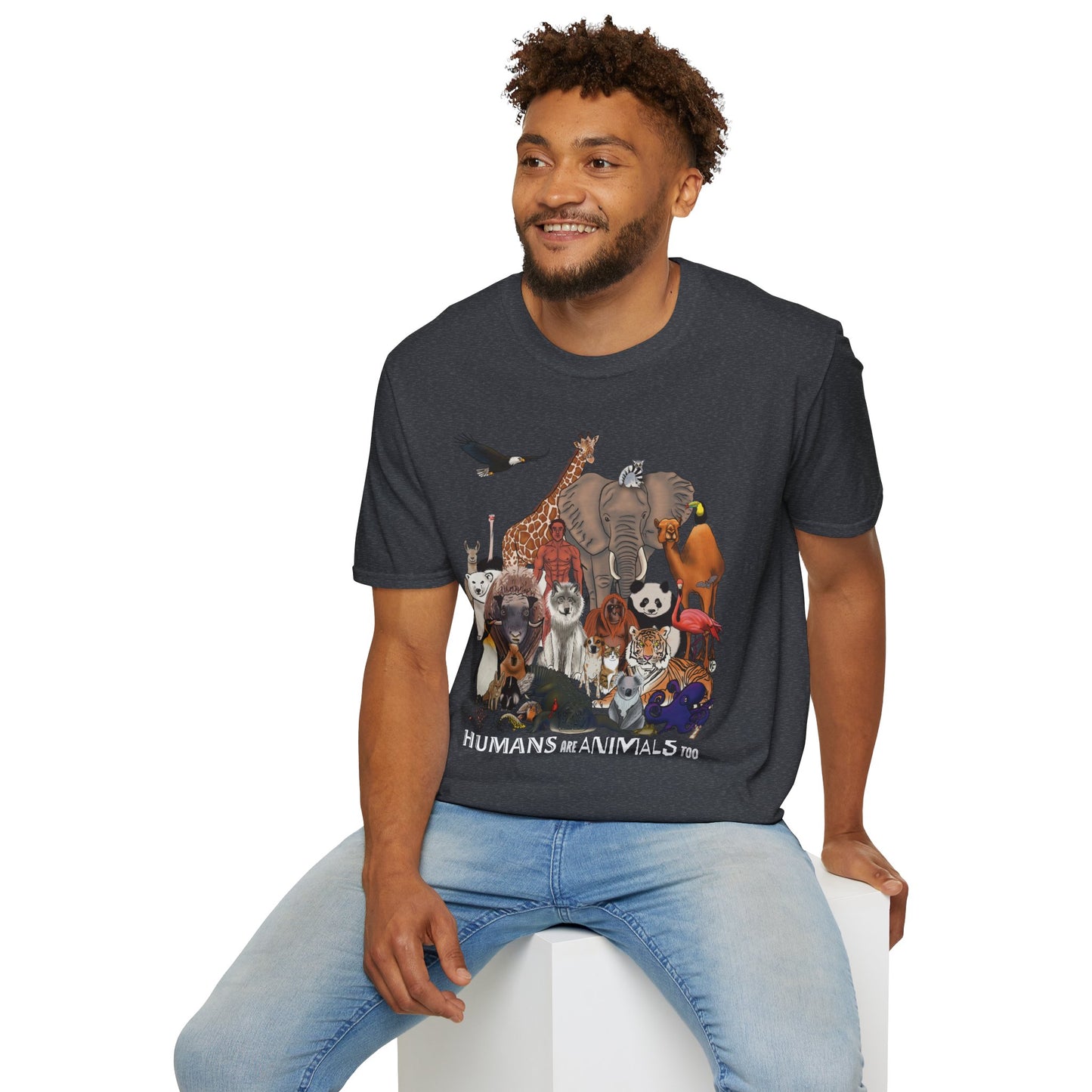 Man wearing a dark grey unisex short sleeve tee featuring a diverse group of illustrated animals—like an elephant, bird, cat, and more—gathered around a human in the center. Below the image, the text reads "humans are animals too," celebrating our place in the animal kingdom with a touch of humor and humility.