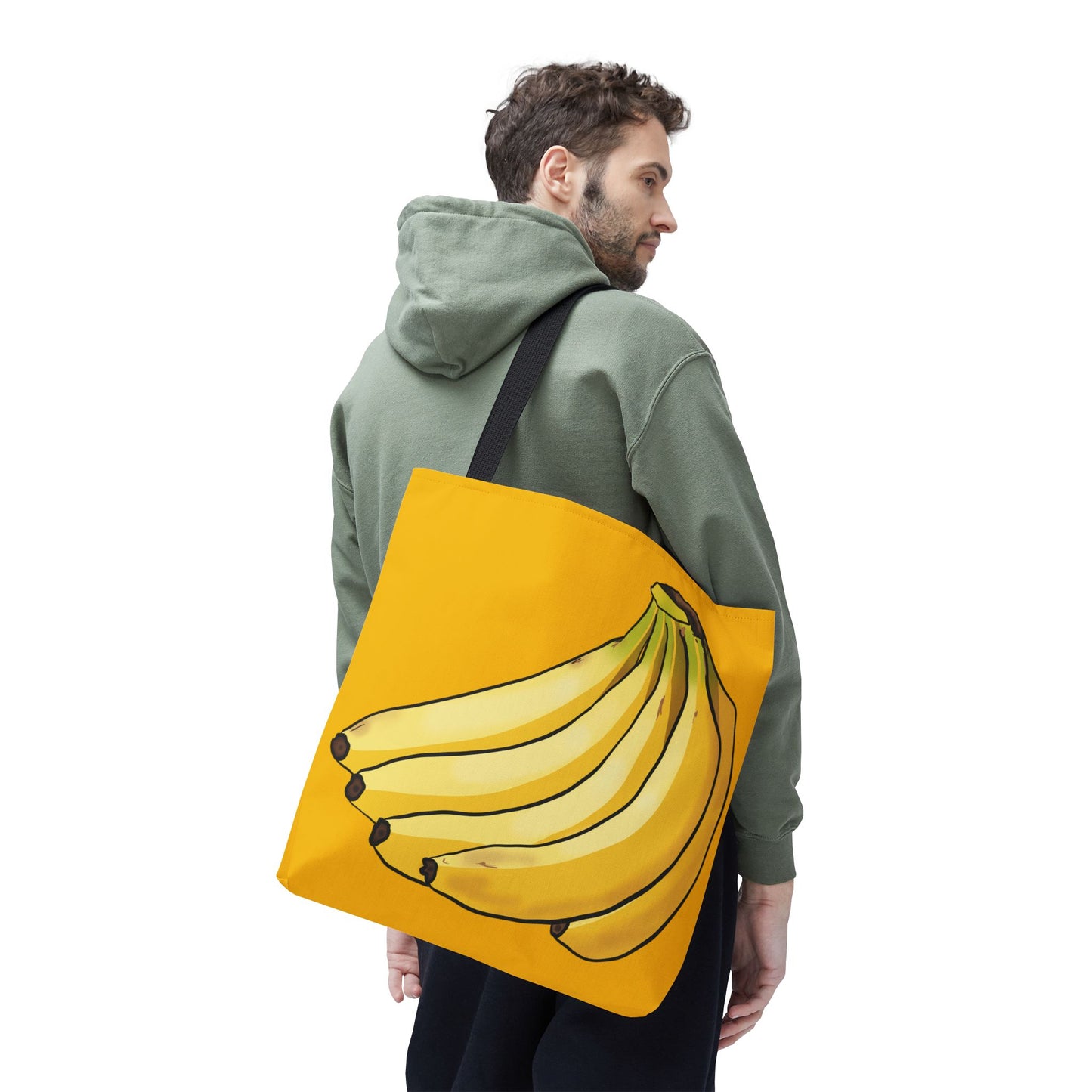 Man carrying a large yellow tote bag featuring a playful illustration of a bunch of bananas on the front, set against a solid yellow background.