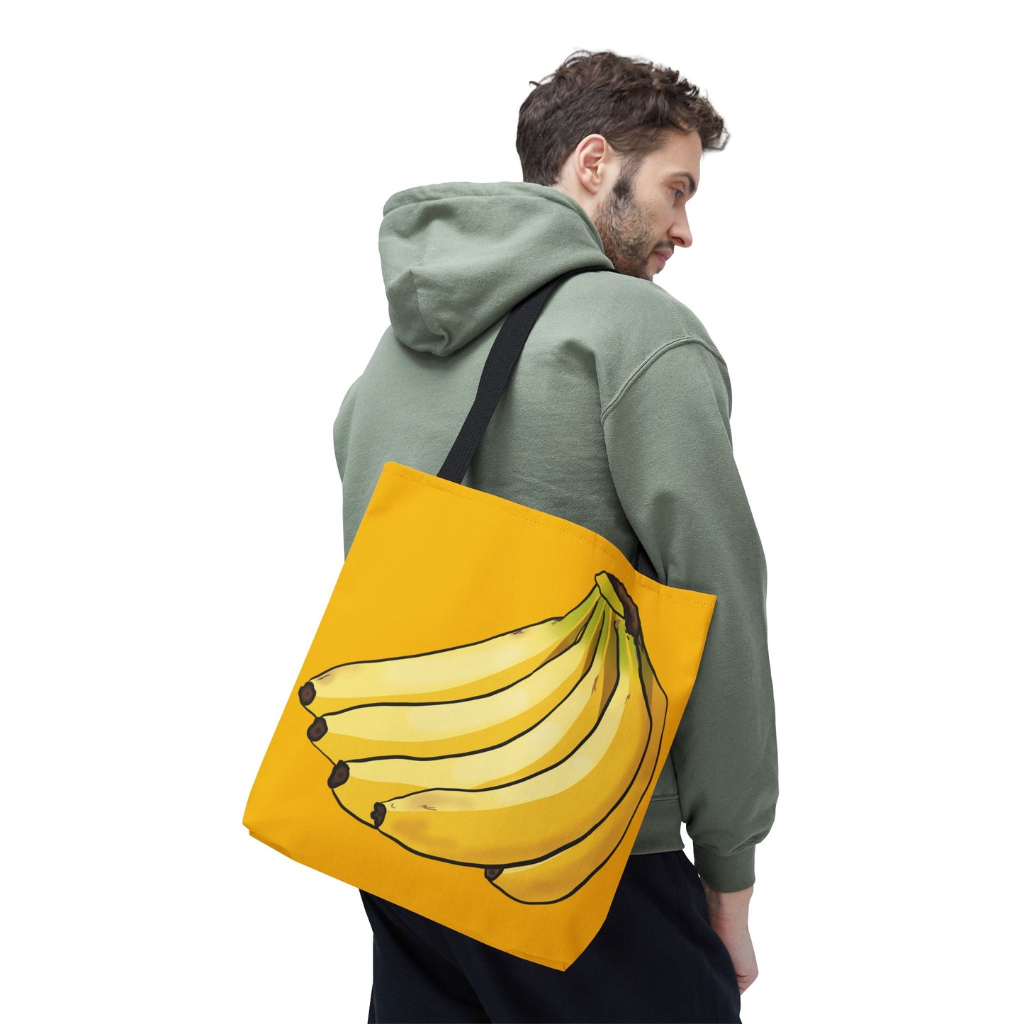 Man carrying a medium yellow tote bag featuring a playful illustration of a bunch of bananas on the front, set against a solid yellow background.