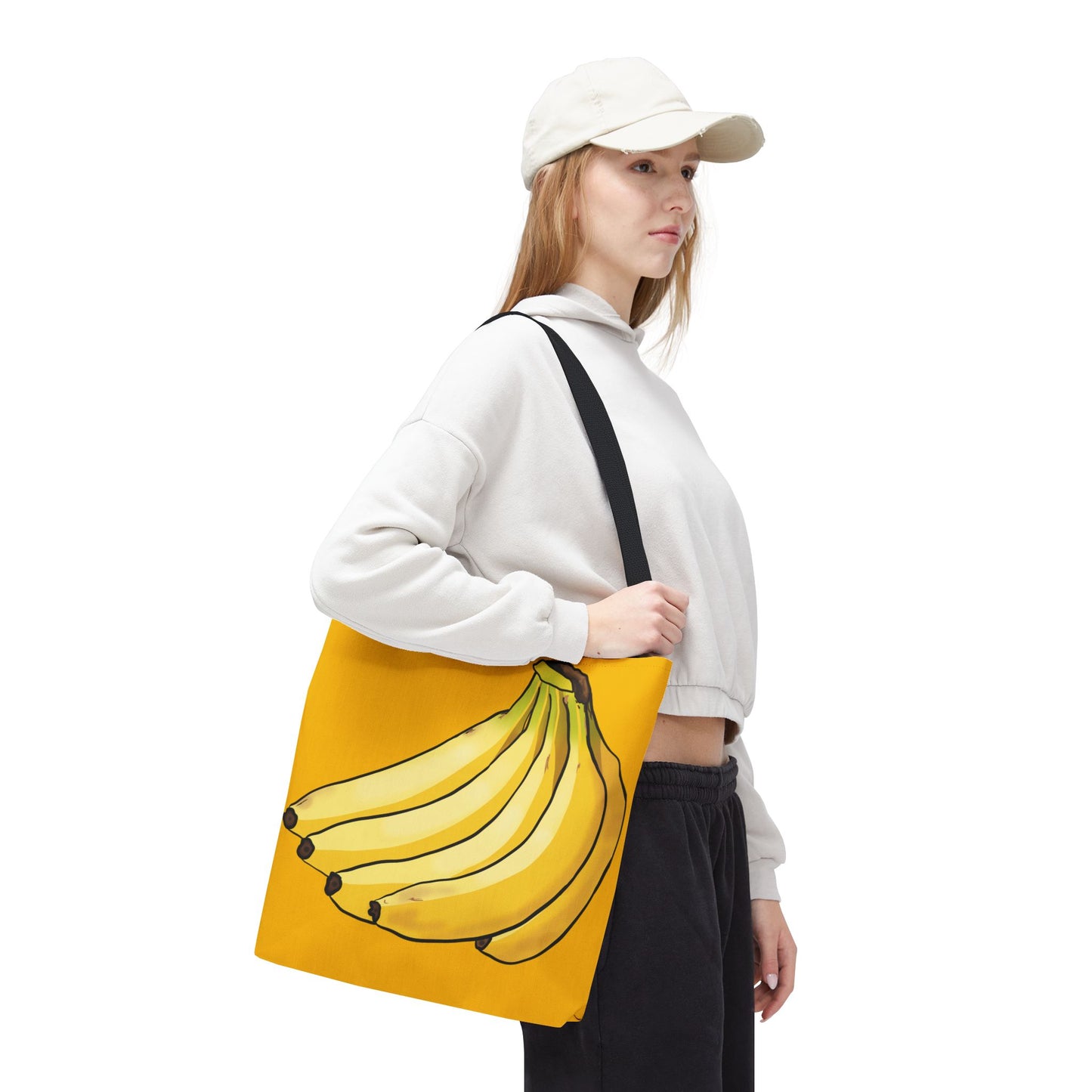 Woman carrying large yellow tote bag featuring a playful illustration of a bunch of bananas on the front, set against a solid yellow background.