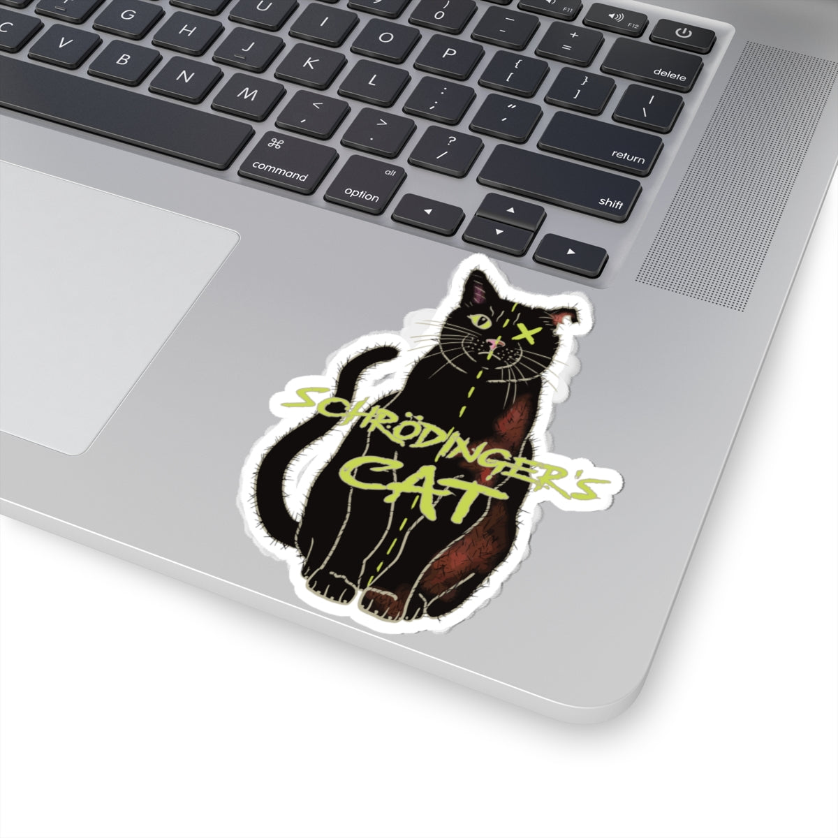 Medium sticker adhered to computer featuring a black cat with one half depicted as alive and the other half as dead, with an X over one eye, representing Schrödinger's cat.