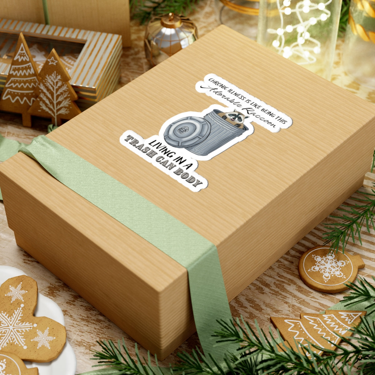 Medium sticker on a gift with a drawing of a raccoon sitting in a metal trash can, accompanied by the text: 'chronic illness is like being this adorable raccoon living in a trash can body.'