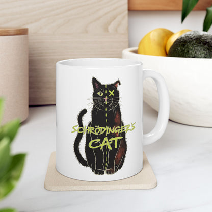 Right view of large white coffee mug featuring a drawing of a black cat that is alive on one half and dead on the other, with the text 'Schrödinger's Cat' printed across the image. The mug is on a coaster on a table next to a bowl of fruit.
