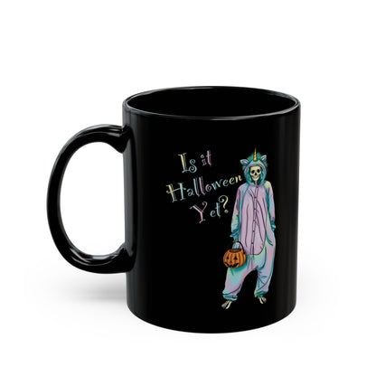 Left view of a small black coffee mug featuring a whimsical illustration of a skeleton dressed in a pastel unicorn onesie, complete with a horn and rainbow accents; the playful text reads "Is it Halloween yet?"—because spooky season should be year-round.