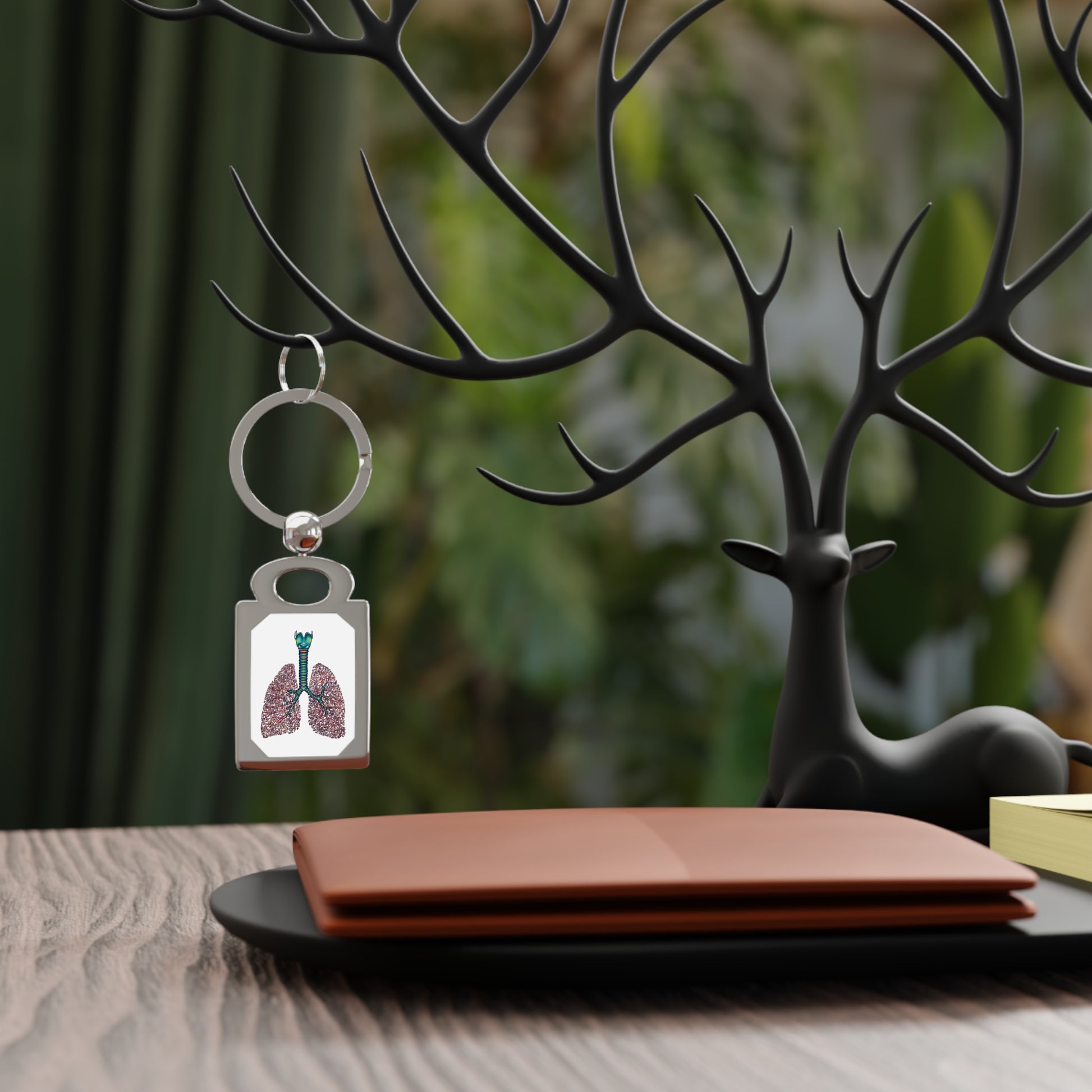 Rectangular silver frame keychain featuring a detailed anatomical drawing of lungs, including the bronchial tree, trachea, and larynx, set against a white background, is hanging on display.