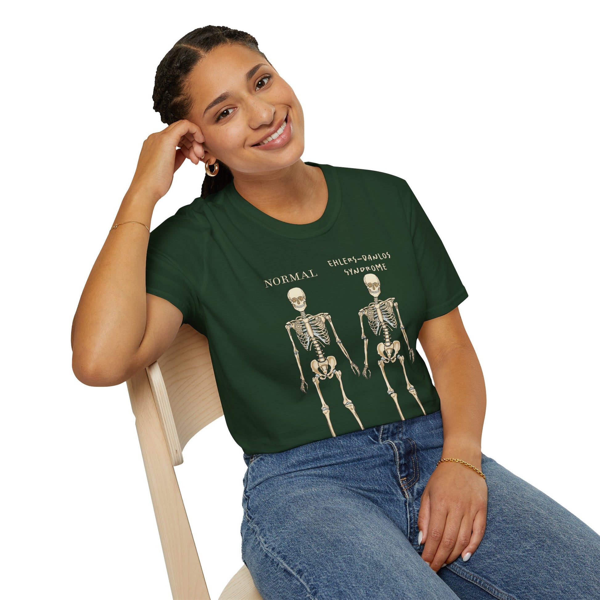 Woman wearing a forest green unisex short sleeve t-shirt featuring two skeletons side by side—one labeled "normal," the other "Ehlers-Danlos Syndrome"—because connective tissue disorders deserve more visibility (and maybe a sense of humor, too).