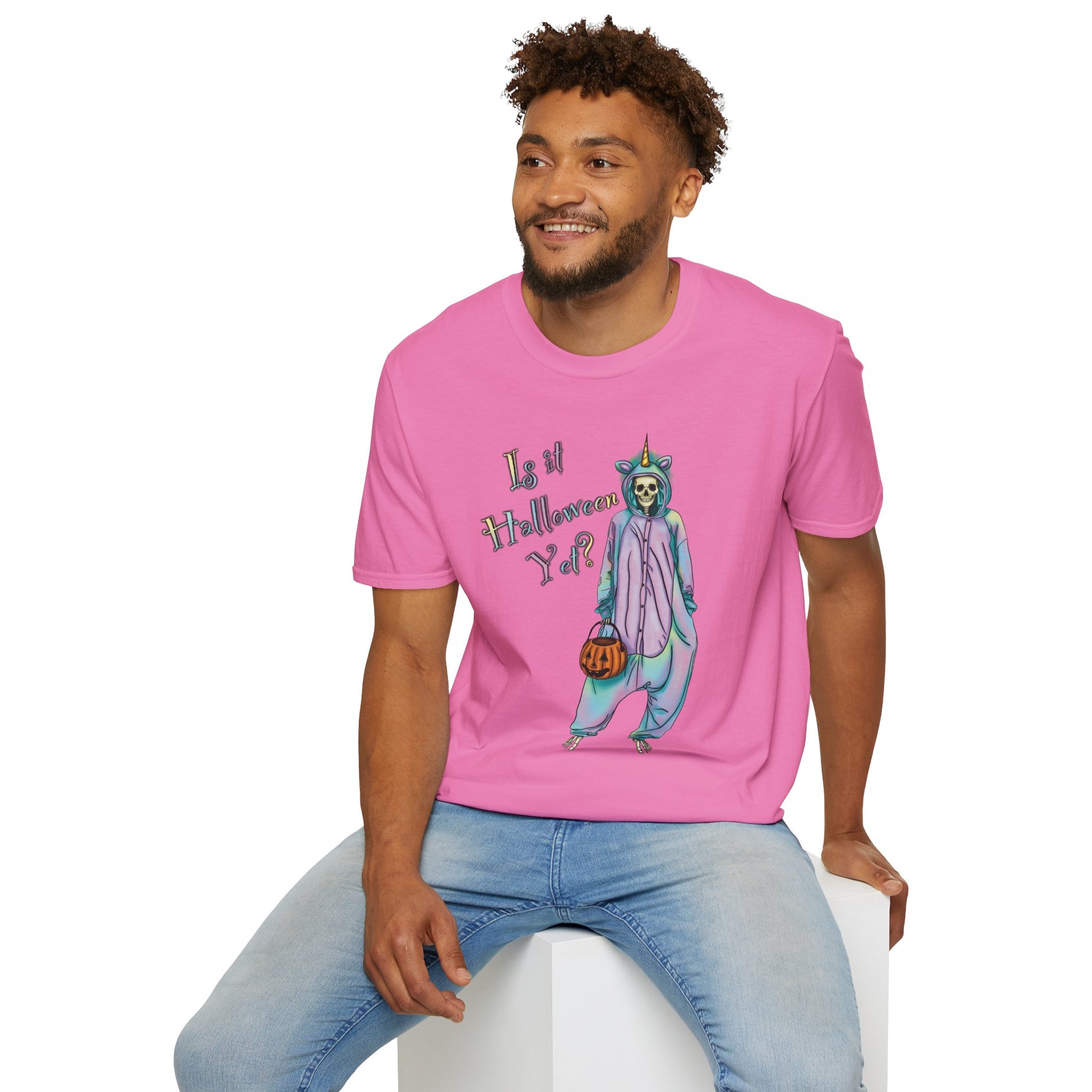 Man wearing a pink t-shirt featuring a drawing of a skeleton in a unicorn costume onesie, with the phrase 'Is it Halloween yet?' printed on it.