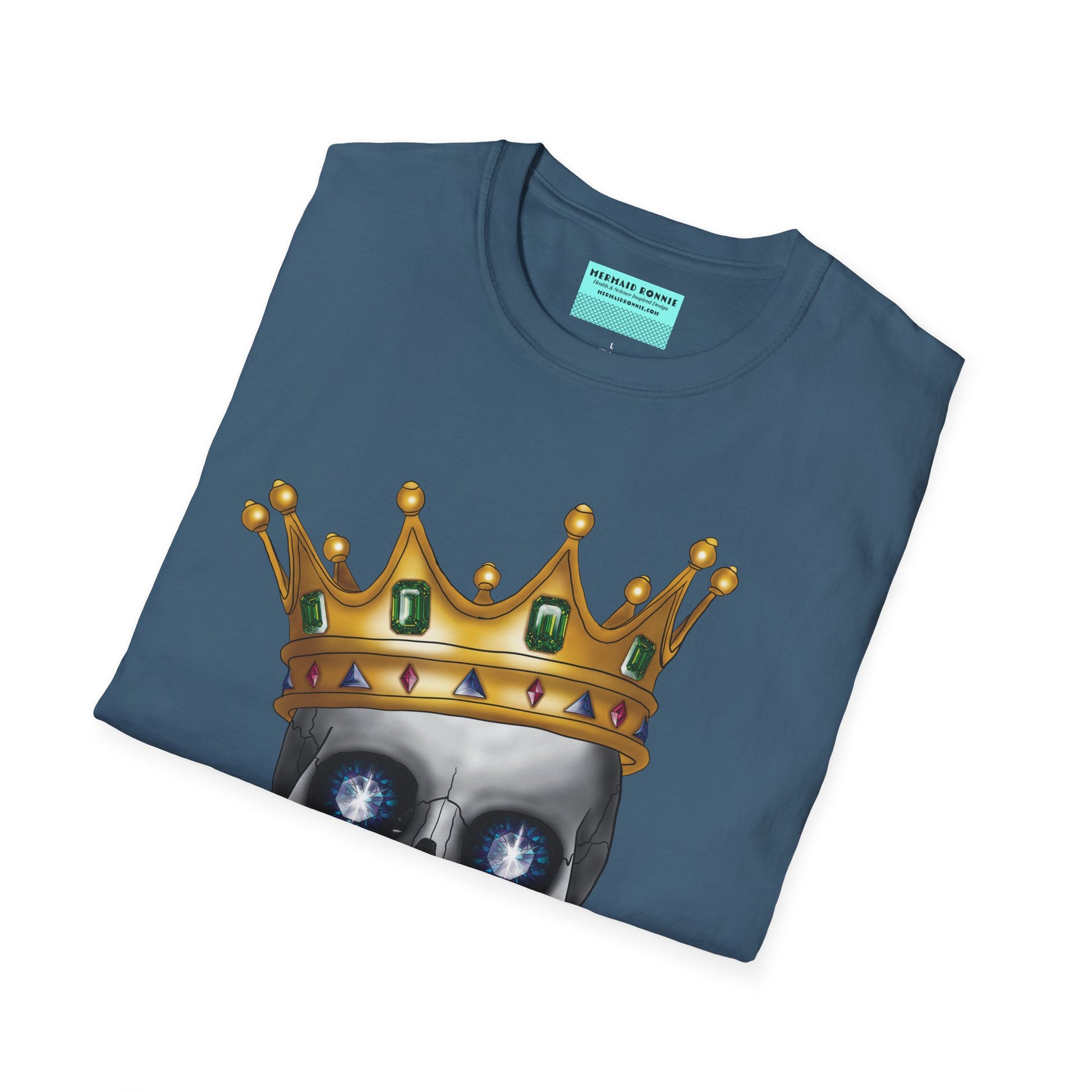 Folded indigo blue t-shirt featuring an anatomical skull wearing an ornate crown, with gold teeth, large sapphire gemstones in the eye sockets, and emeralds and rubies decorating the crown.