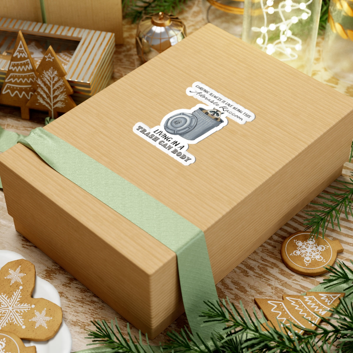 Small sticker on a gift with a drawing of a raccoon sitting in a metal trash can, accompanied by the text: 'chronic illness is like being this adorable raccoon living in a trash can body.'