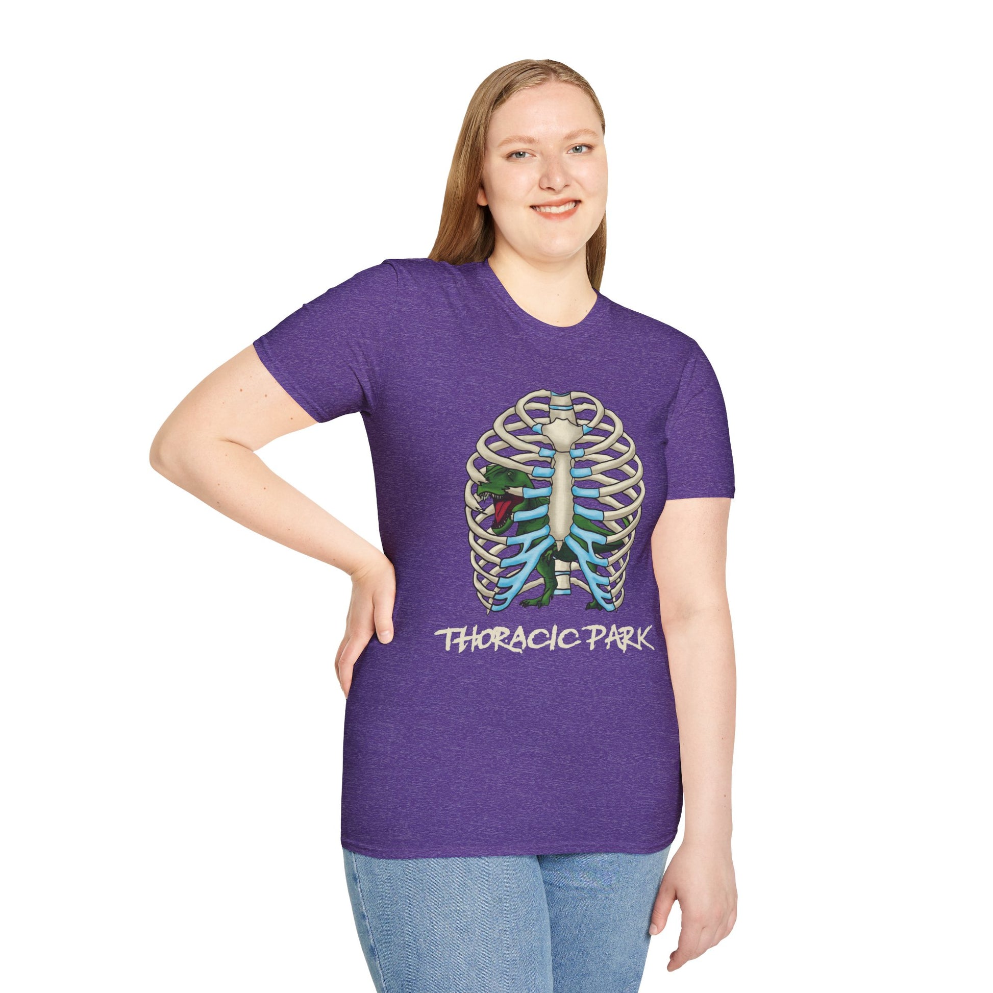 Woman wearing a purple unisex short sleeve tee with a clever Jurassic twist—an anatomical rib cage doubles as a prehistoric prison for a tiny T-Rex, with the punny caption "Thoracic Park" below. It's dino-mite meets anatomy class in the best way possible.