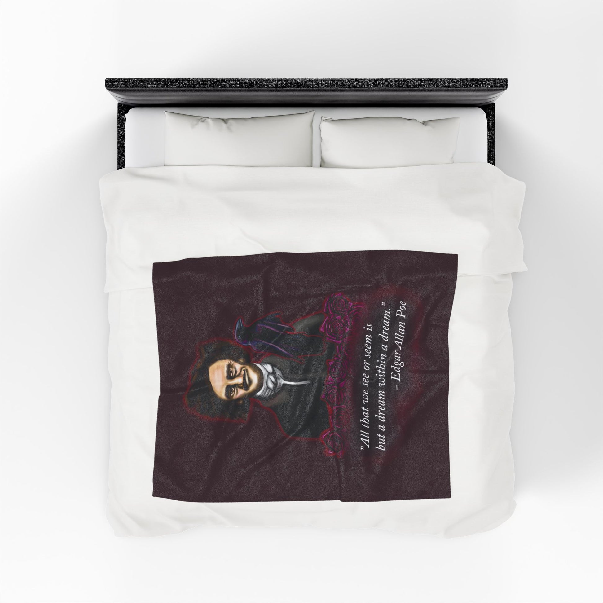 A medium burgundy velveteen plush blanket featuring a smirking Edgar Allan Poe, a brooding raven, and crimson roses—perfect for cozying up with your favorite haunting thoughts and the poetic quote, "All that we see or seem is but a dream within a dream. Shown on a queen size bed from above.
