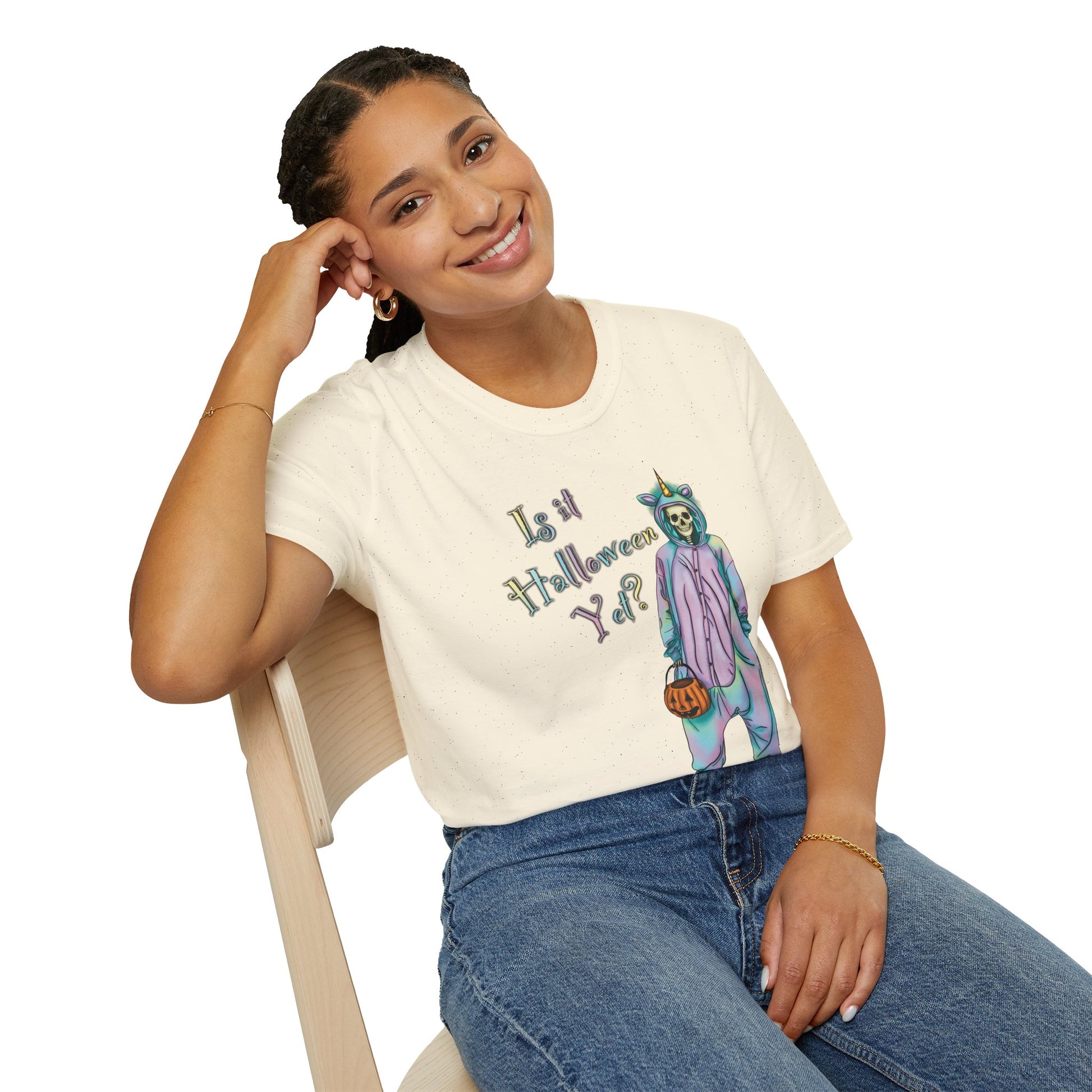 Woman wearing a beige t-shirt featuring a drawing of a skeleton in a unicorn costume onesie, with the phrase 'Is it Halloween yet?' printed on it.