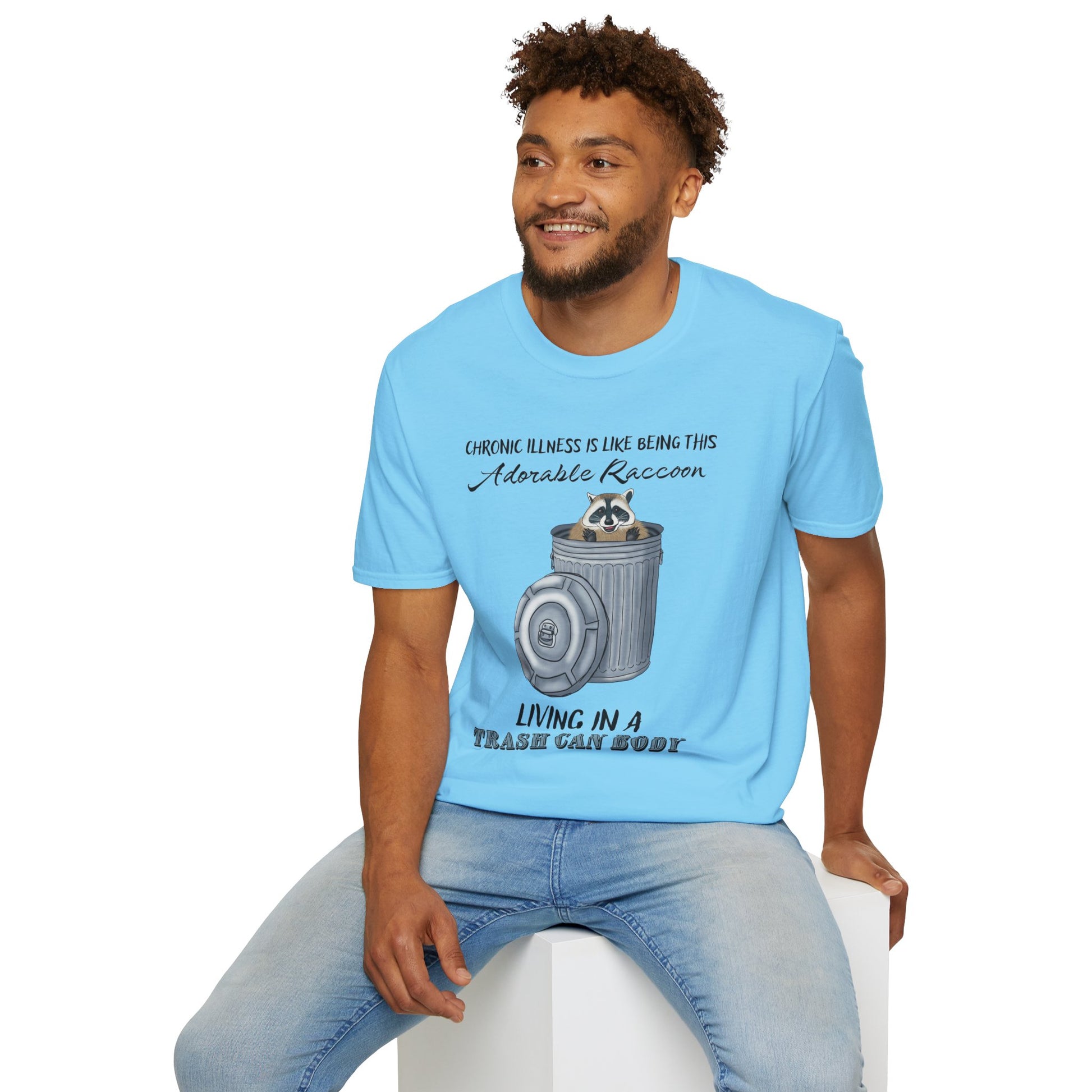 Man wearing a sky blue t-shirt featuring a picture of a raccoon in a metal trash can, with the phrase 'Chronic illness is like being this adorable raccoon living in a trash can body' printed on it.