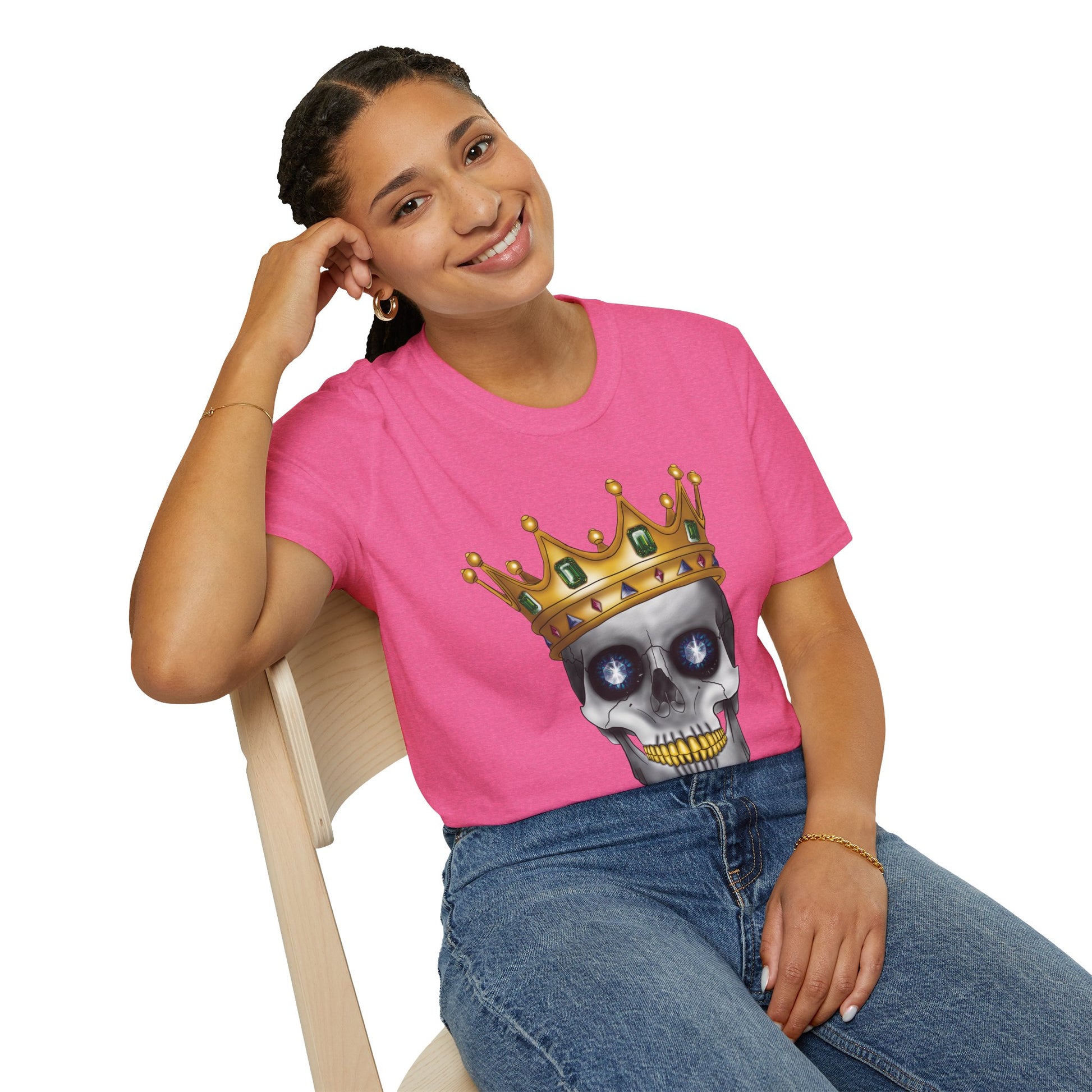 Woman wearing a pink t-shirt featuring an anatomical skull wearing an ornate crown, with gold teeth, large sapphire gemstones in the eye sockets, and emeralds and rubies decorating the crown.