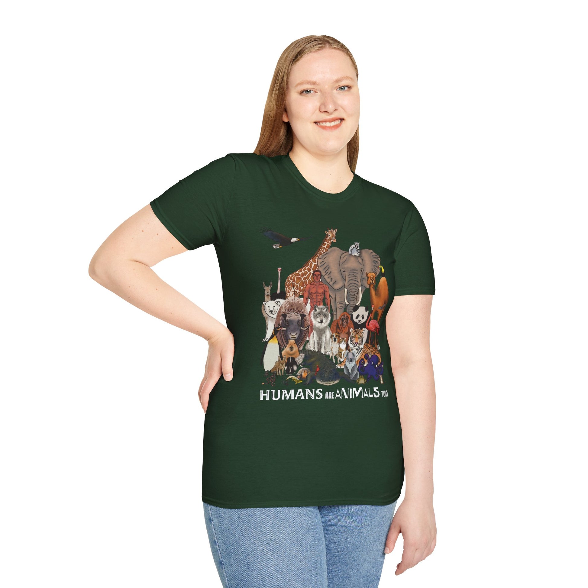 Woman wearing a green unisex short sleeve tee featuring a diverse group of illustrated animals—like an elephant, bird, cat, and more—gathered around a human in the center. Below the image, the text reads "humans are animals too," celebrating our place in the animal kingdom with a touch of humor and humility.