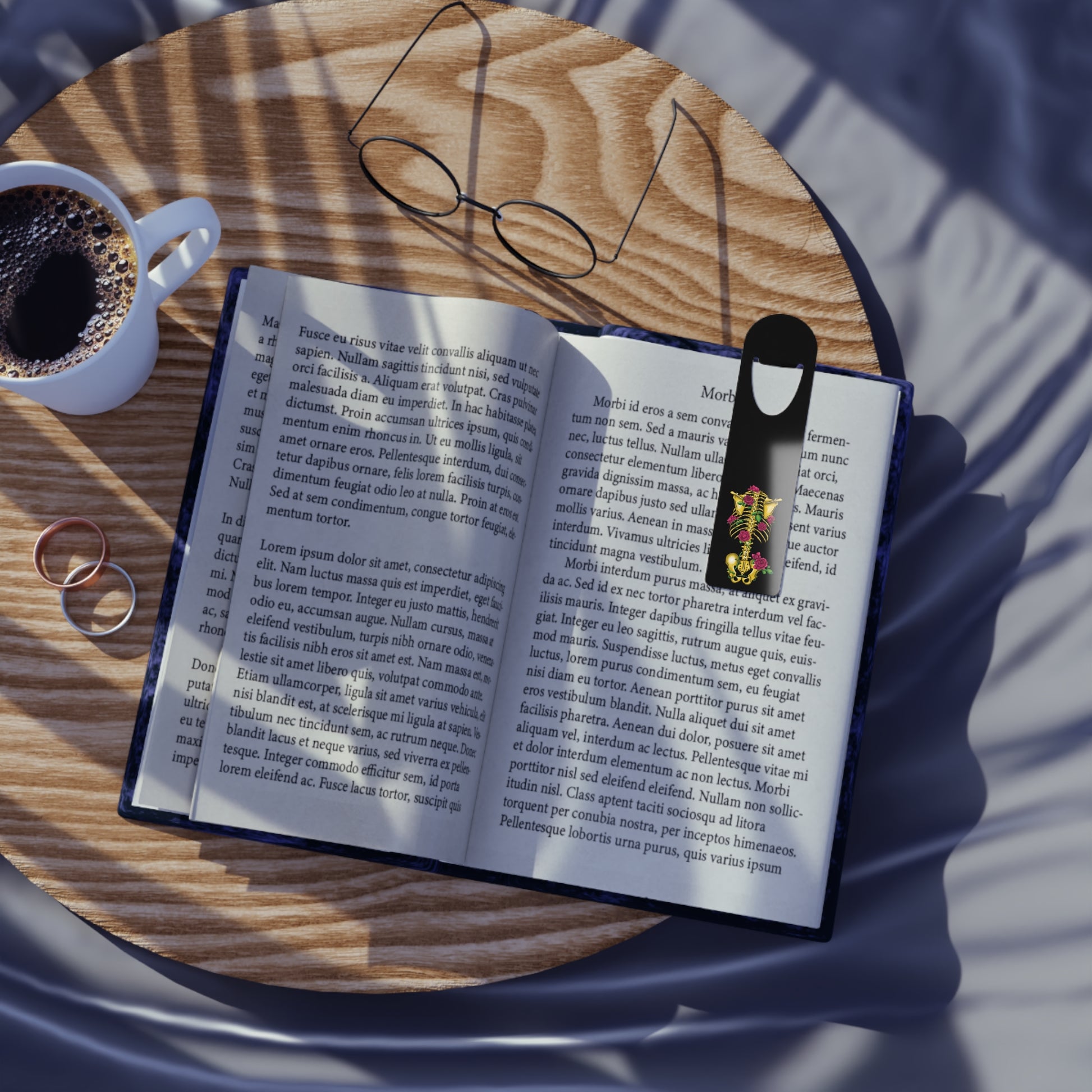 Black aluminum bookmark in use featuring a gold anatomical skeleton with vibrant pink roses entwined around the bones, creating a striking blend of macabre and botanical elegance.