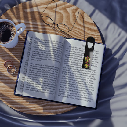 Black aluminum bookmark in use featuring a gold anatomical skeleton with vibrant pink roses entwined around the bones, creating a striking blend of macabre and botanical elegance.