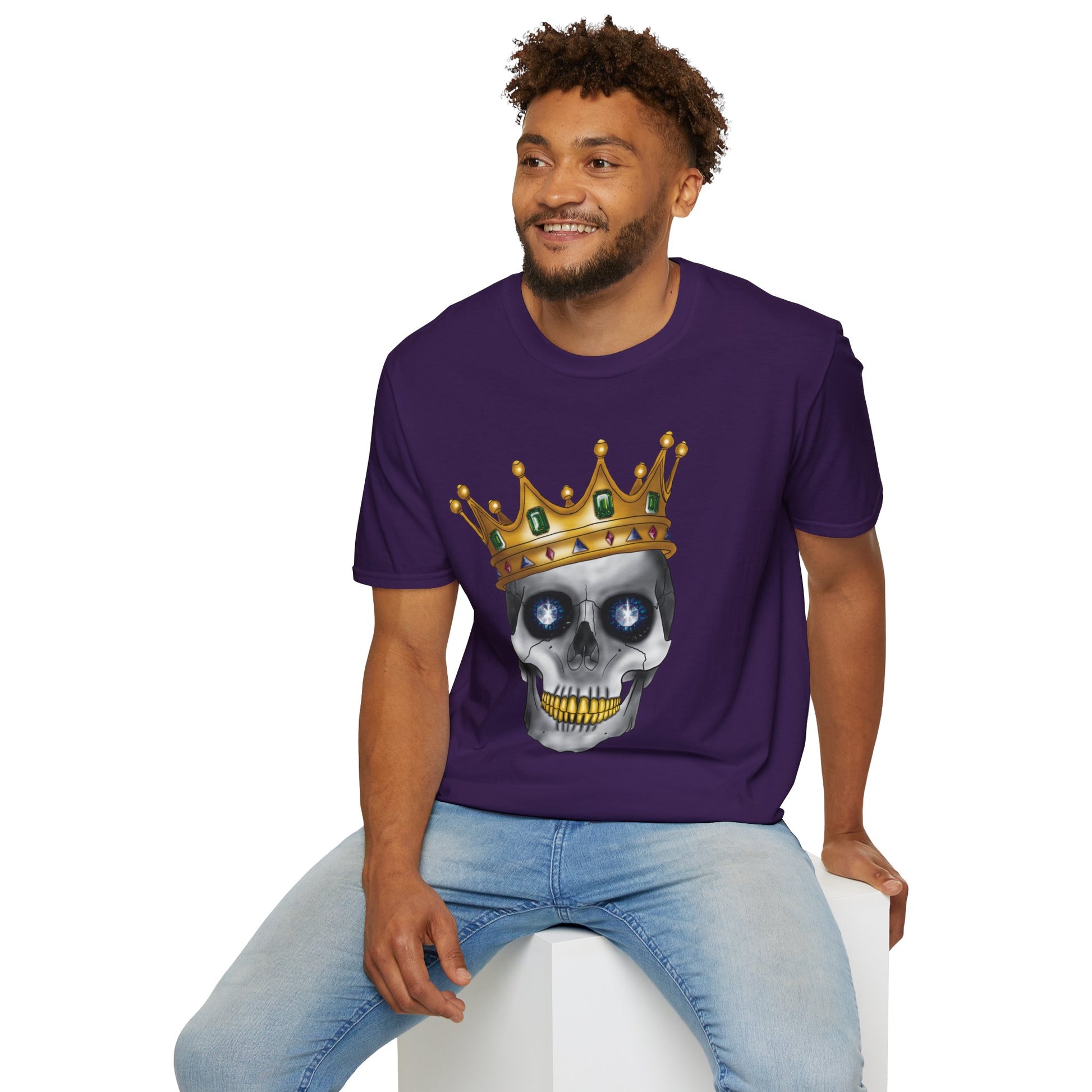 Man wearing a purple t-shirt featuring an anatomical skull wearing an ornate crown, with gold teeth, large sapphire gemstones in the eye sockets, and emeralds and rubies decorating the crown.
